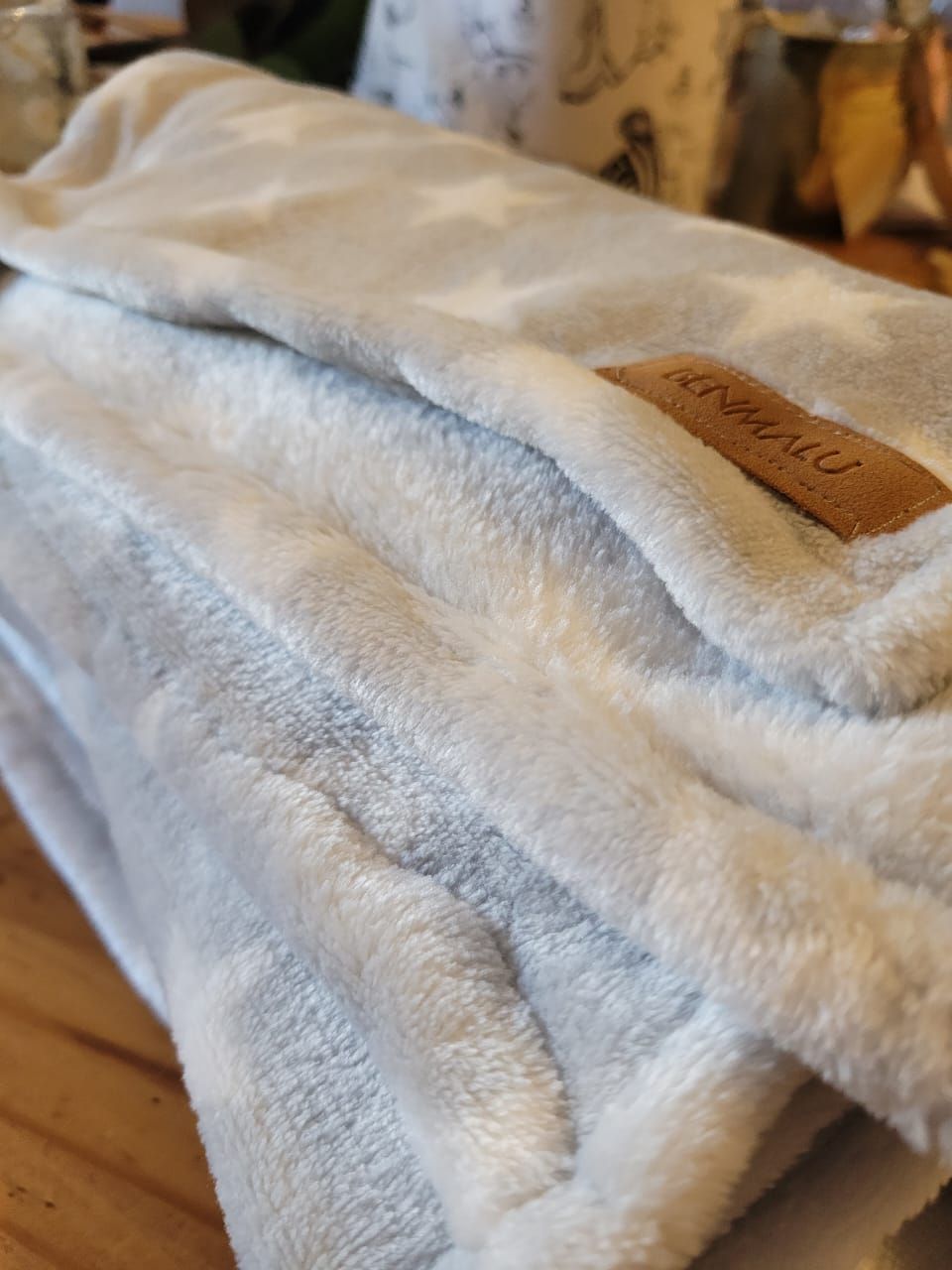Manta suave de forro polar azul claro con una etiqueta marrón colocada sobre una cama o sofá.