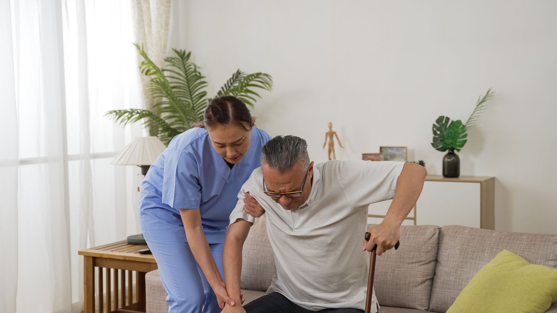 An in-home care attendant is helping a senior male stand up. An in-home care attendant is helping a senior male stand up.