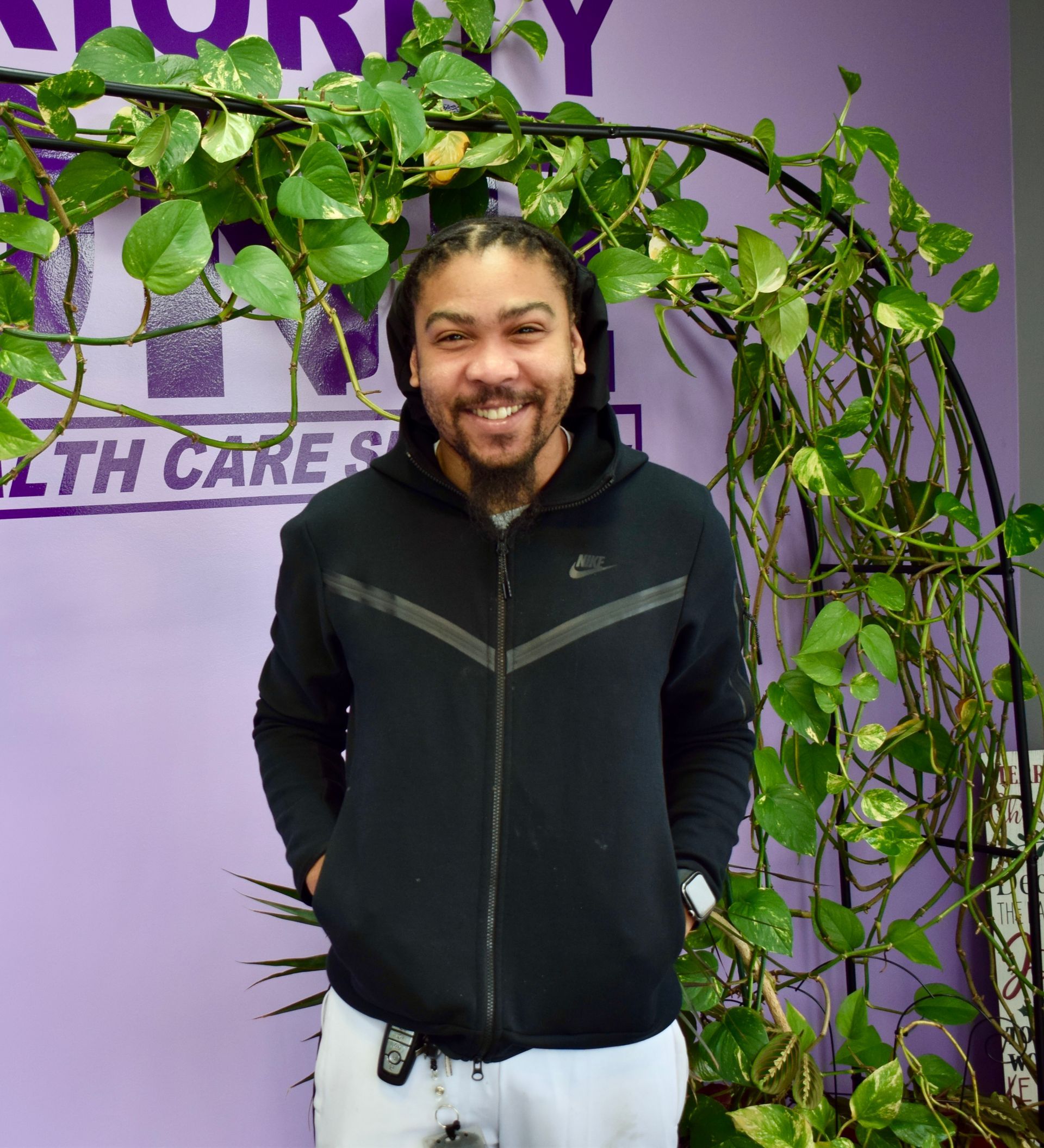 A Man in A Black Nike Jacket Is Standing in Front of A Purple Wall.