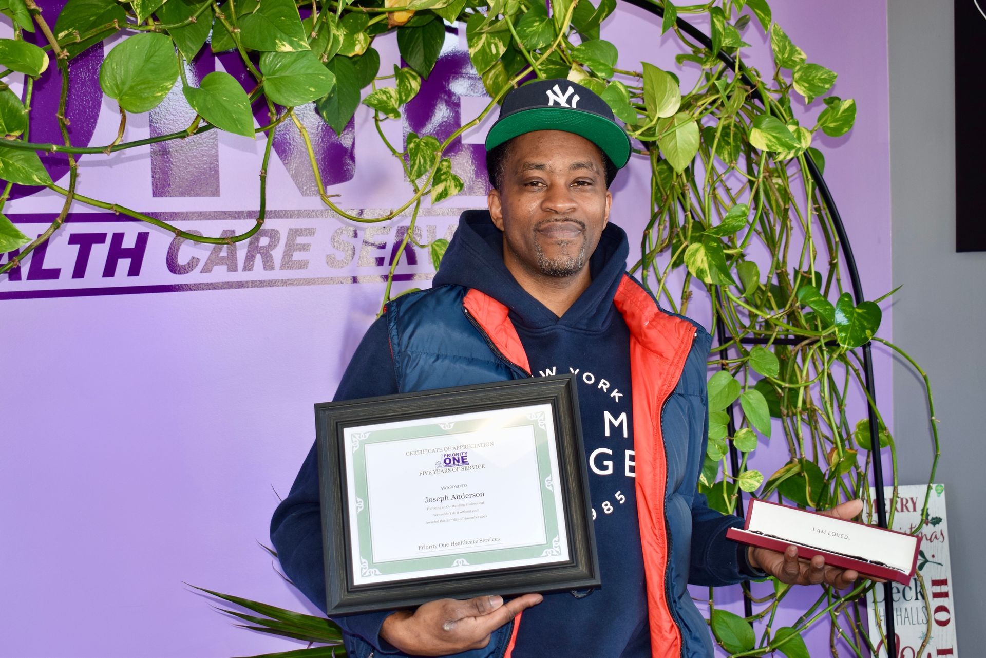 A Man Is Holding Two Certificates in Front of A Purple Wall.