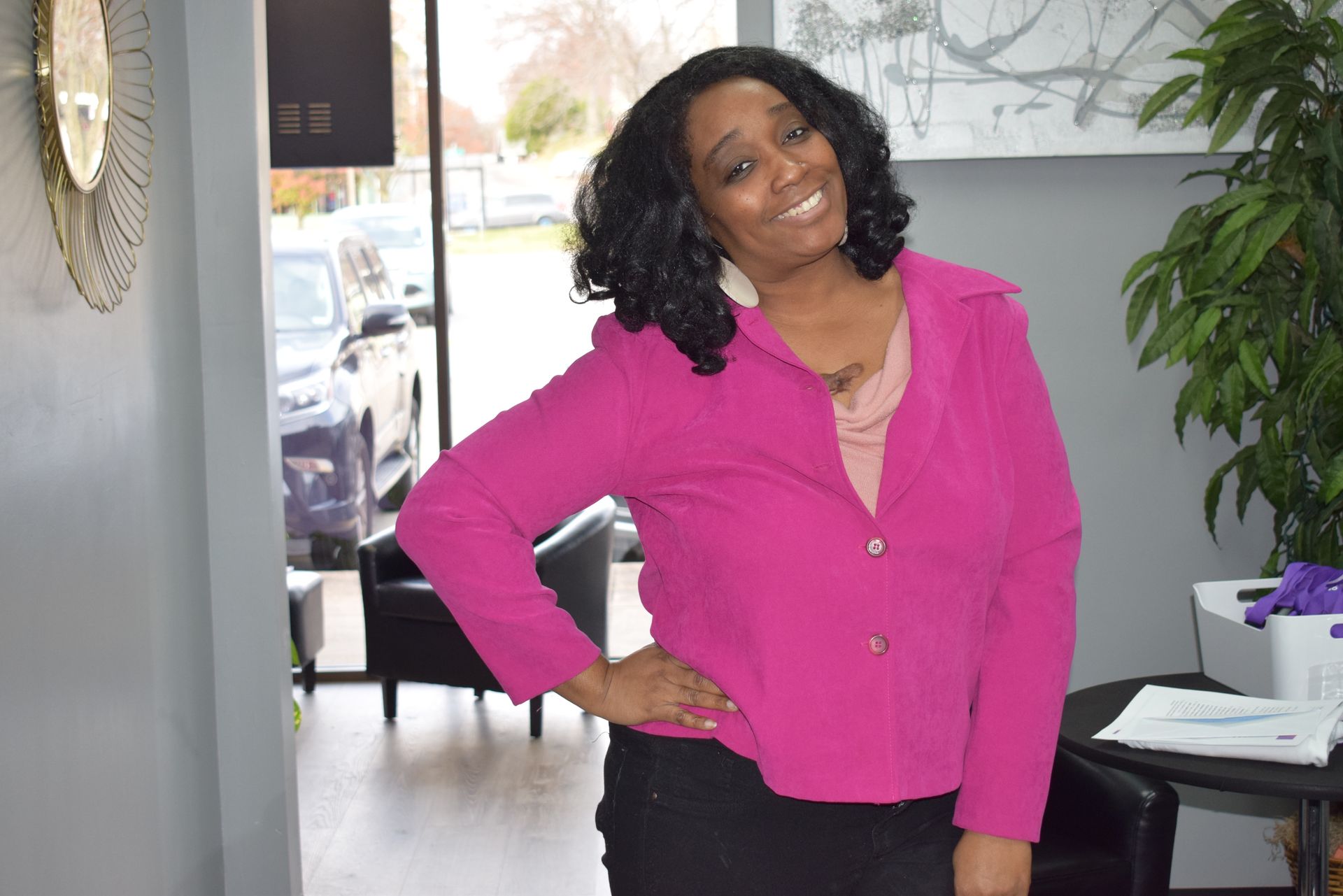 A Woman in A Pink Jacket Is Standing in A Room with Her Hands on Her Hips.