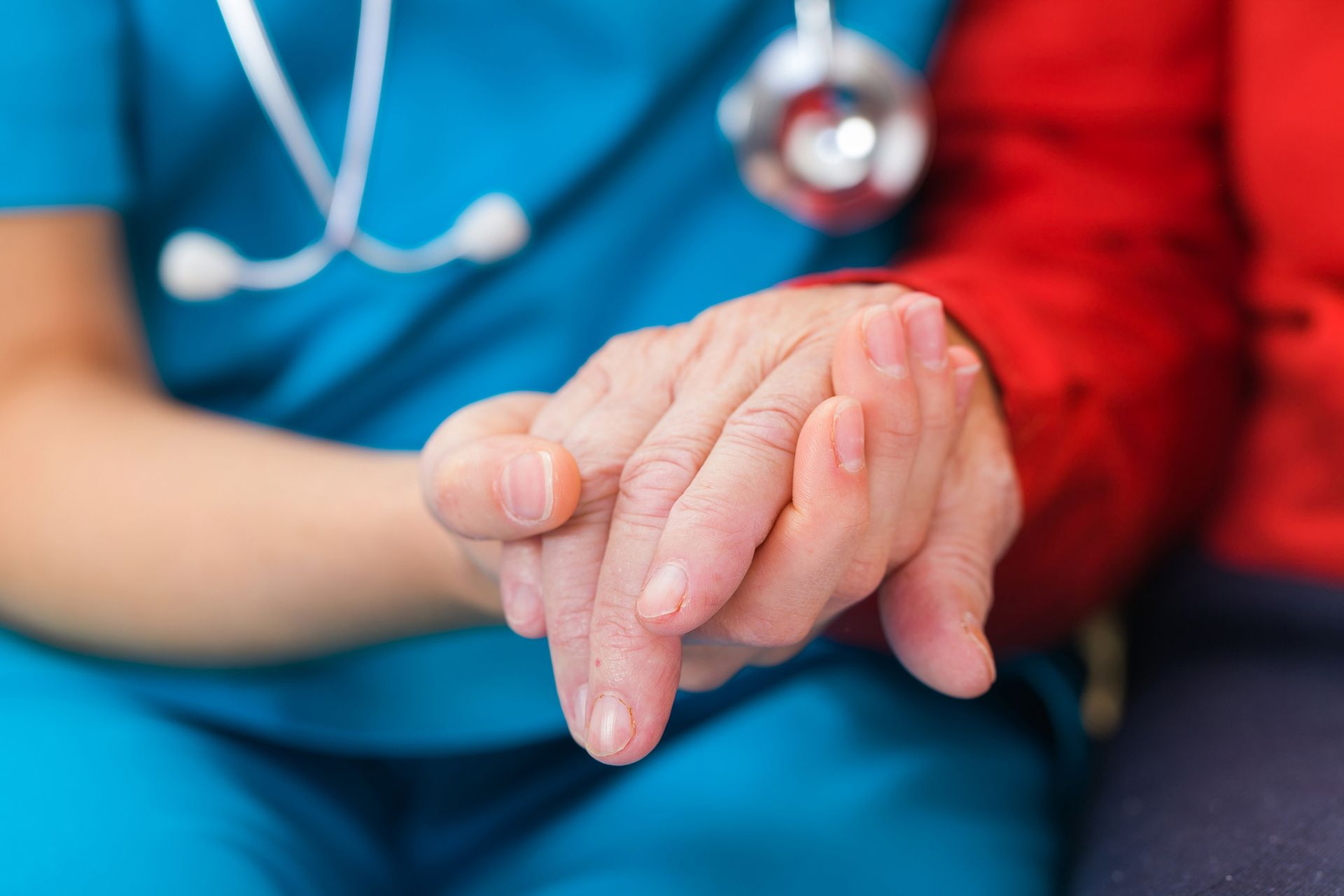 Healthcare worker comforting elderly patient with hand-holding in hospital setting for senior care.