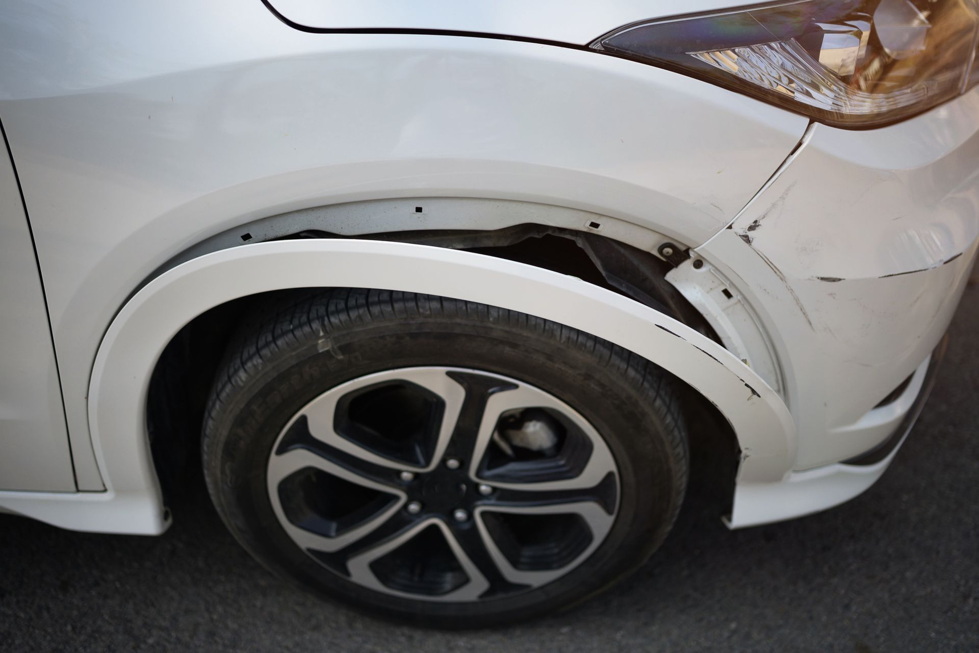 White car with damaged front fender above the wheel.
