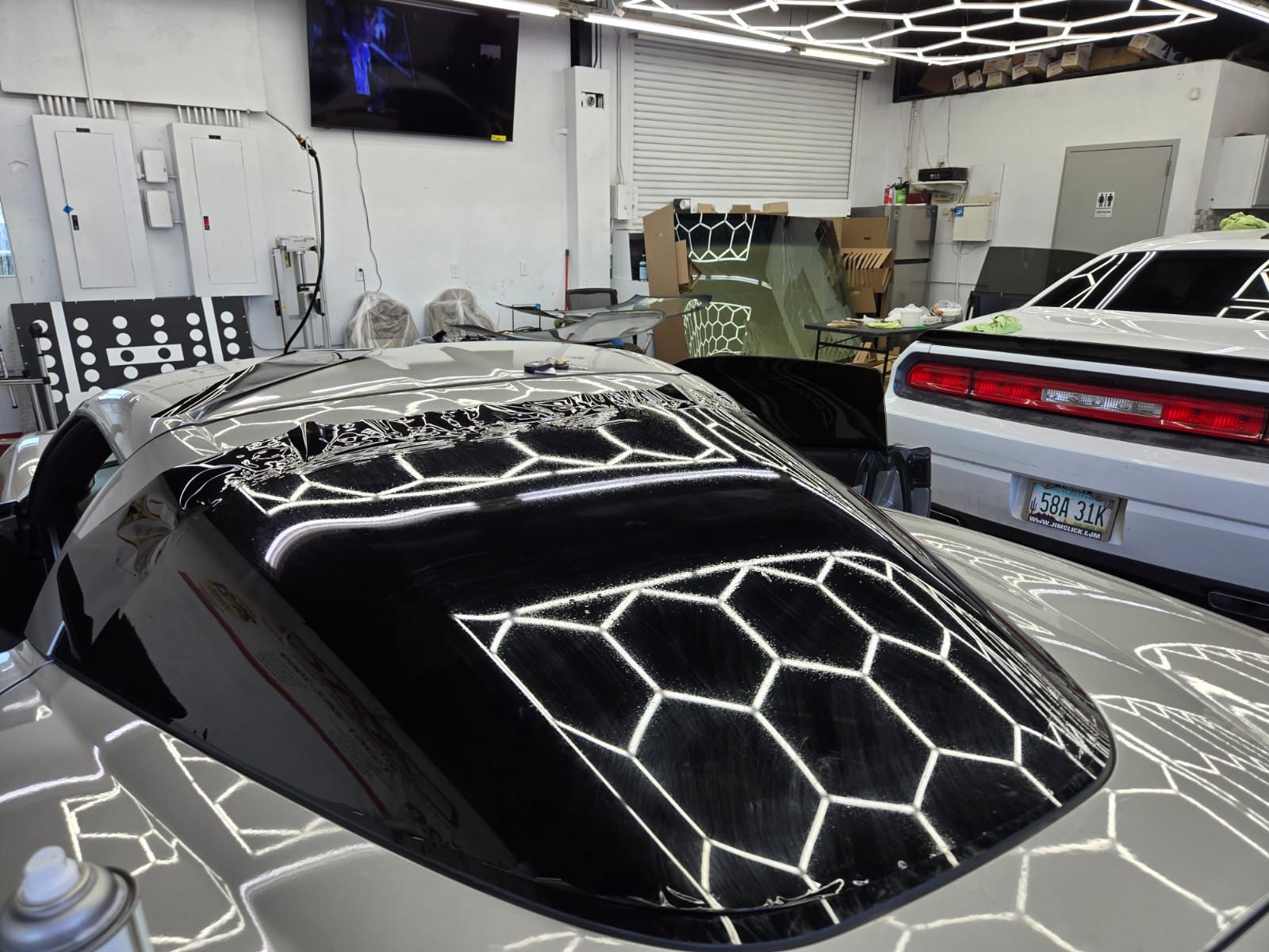 Black car hood with honeycomb reflections, in a well-lit garage, next to a white car.