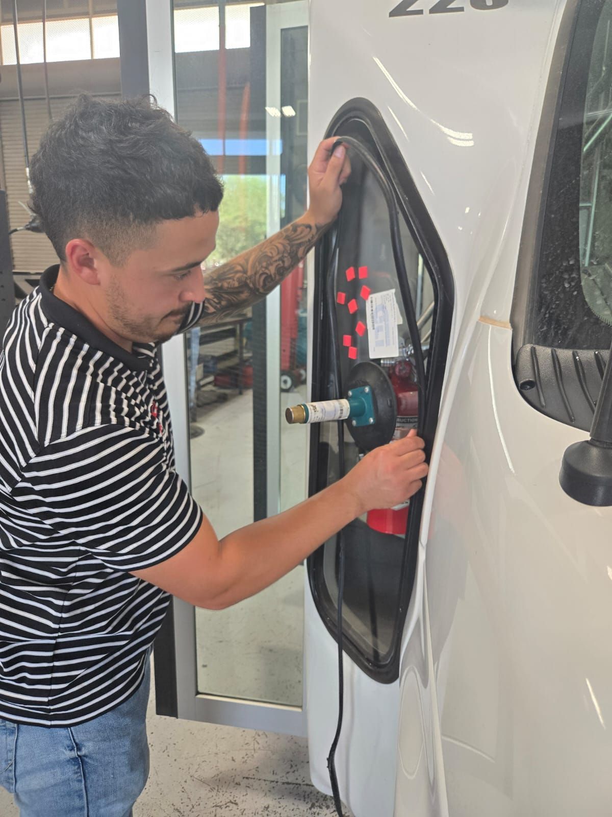 Man installing a window on a white vehicle; shop setting.