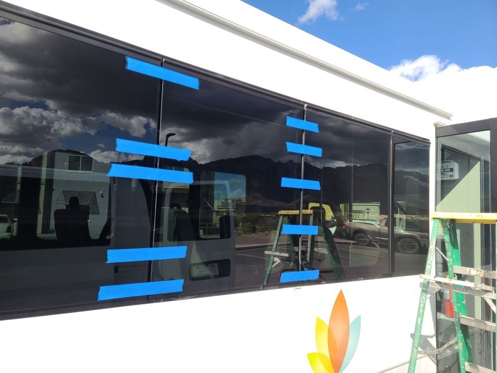 Large window with blue tape, reflecting mountains and vehicles, next to a ladder.