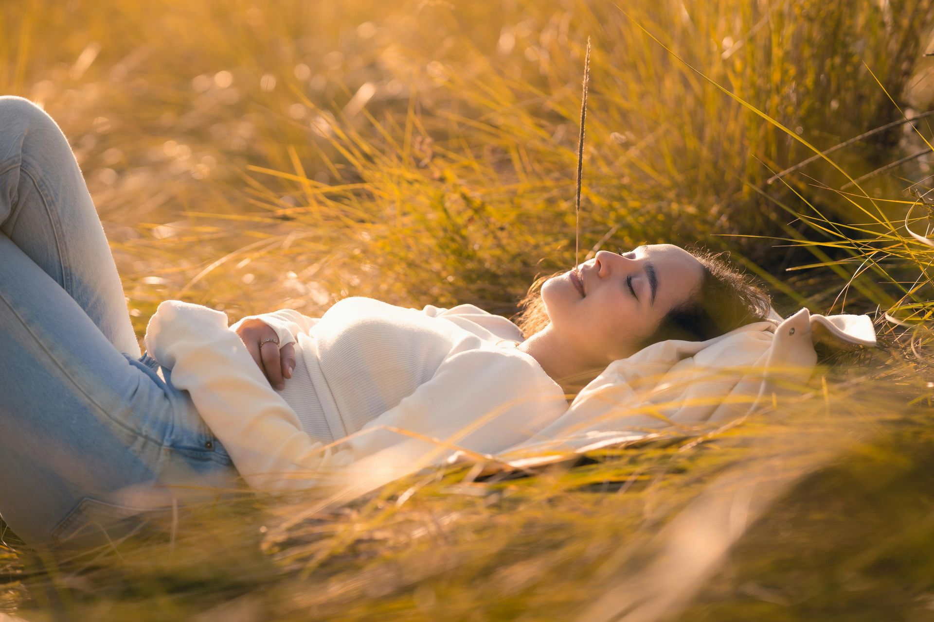 A stack of three books topped with a small sculpture sits next to a glowing candle and hands typing on a laptop.