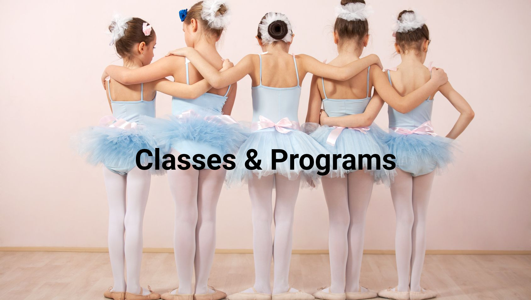 Children in pink ballet leotards holding the barre and lifting a leg in a dance studio