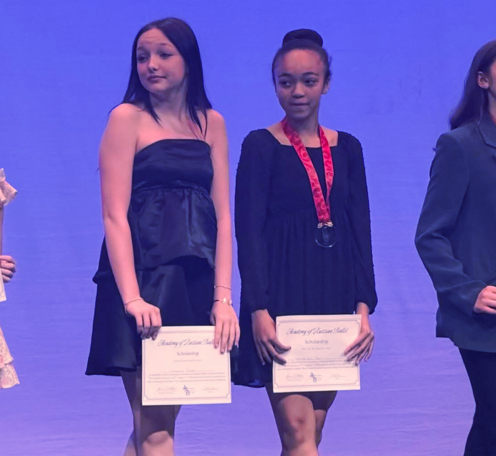 Two people on a stage hold certificates under purple lighting