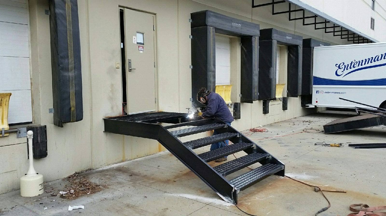 A man is welding a set of stairs outside of a building.