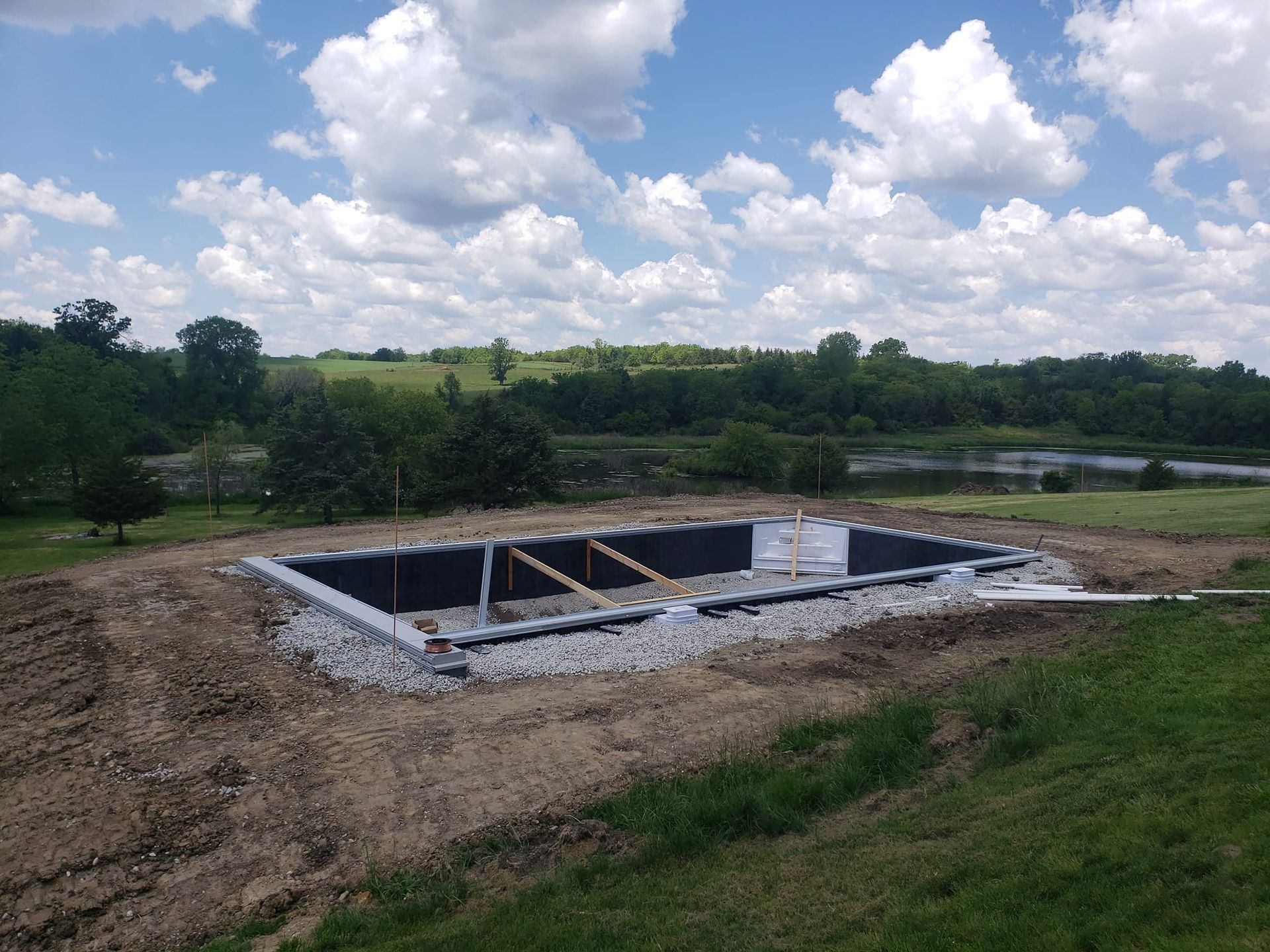 A swimming pool is being built in a field with a lake in the background.