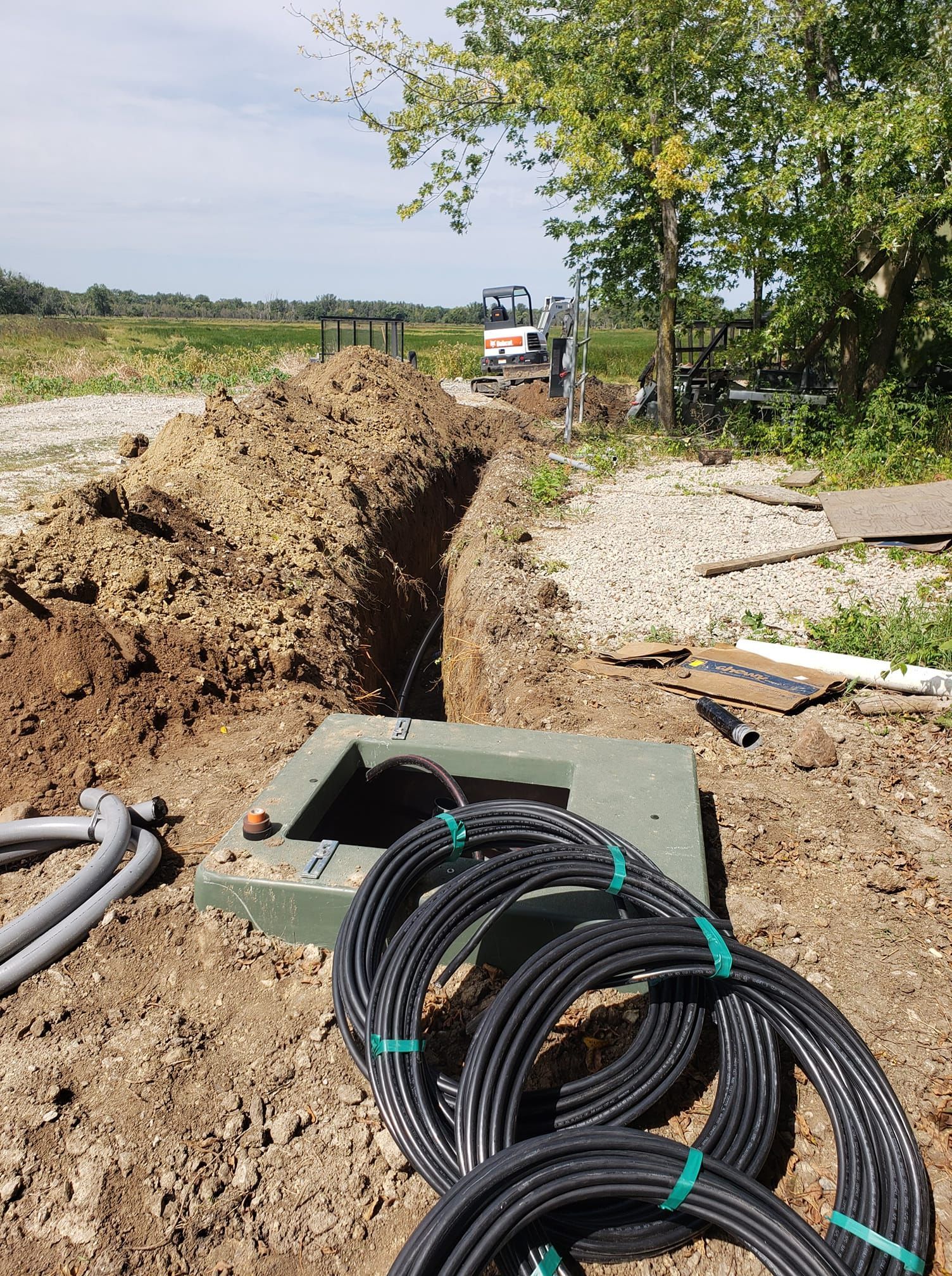 A bunch of wires are laying in the dirt next to a hole in the ground.