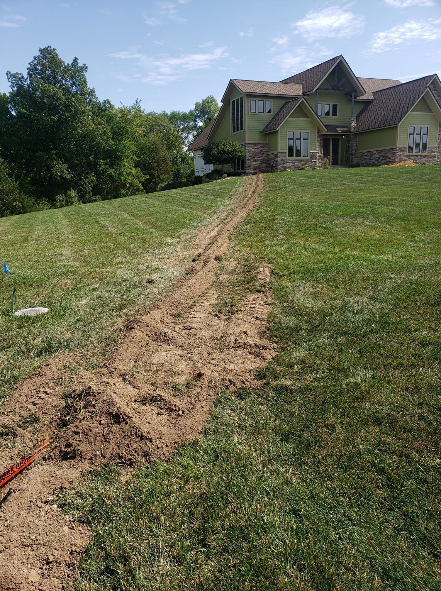 A dirt path leading to a large house in the middle of a lush green field.