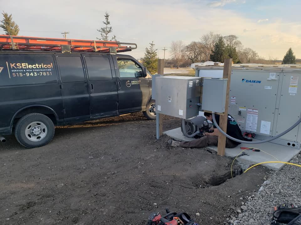A black van is parked in a dirt lot next to a man working on a machine.