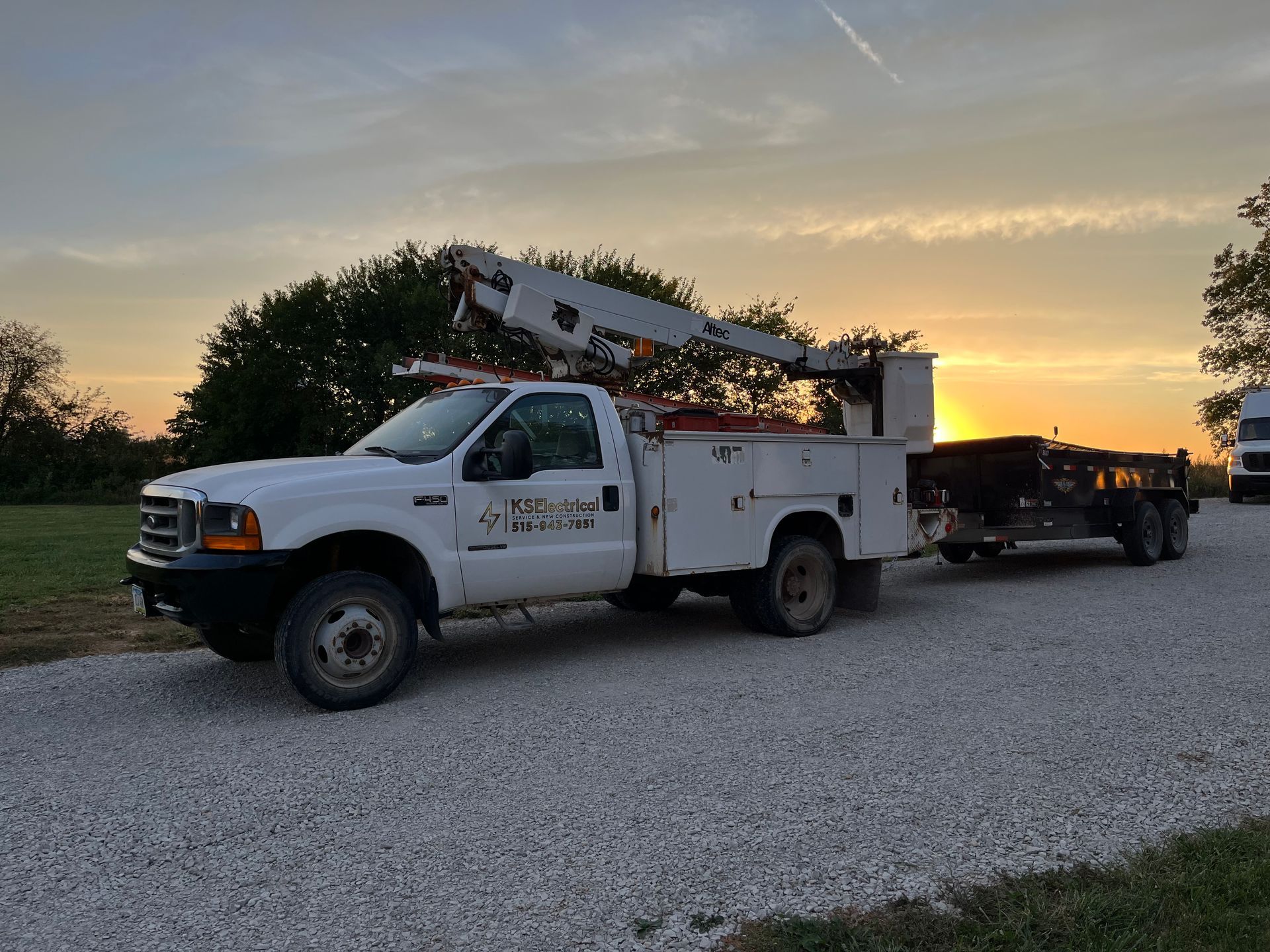 A white truck with a crane on top of it is parked in a gravel lot.