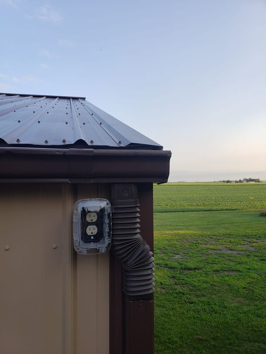 A drainpipe is attached to the side of a building next to a field.