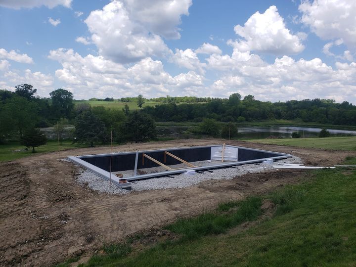 A swimming pool is being built in a field with a lake in the background.