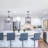 A kitchen with white cabinets , stainless steel appliances , a large island and stools.