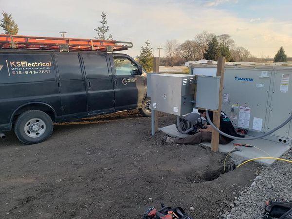 A black van is parked next to a man working on a machine.