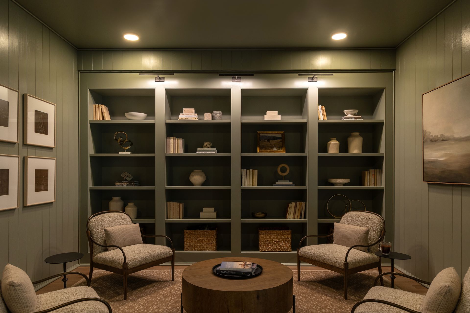Cozy reading nook with built-in bookshelves, armchairs, and a round coffee table in an olive-green room.