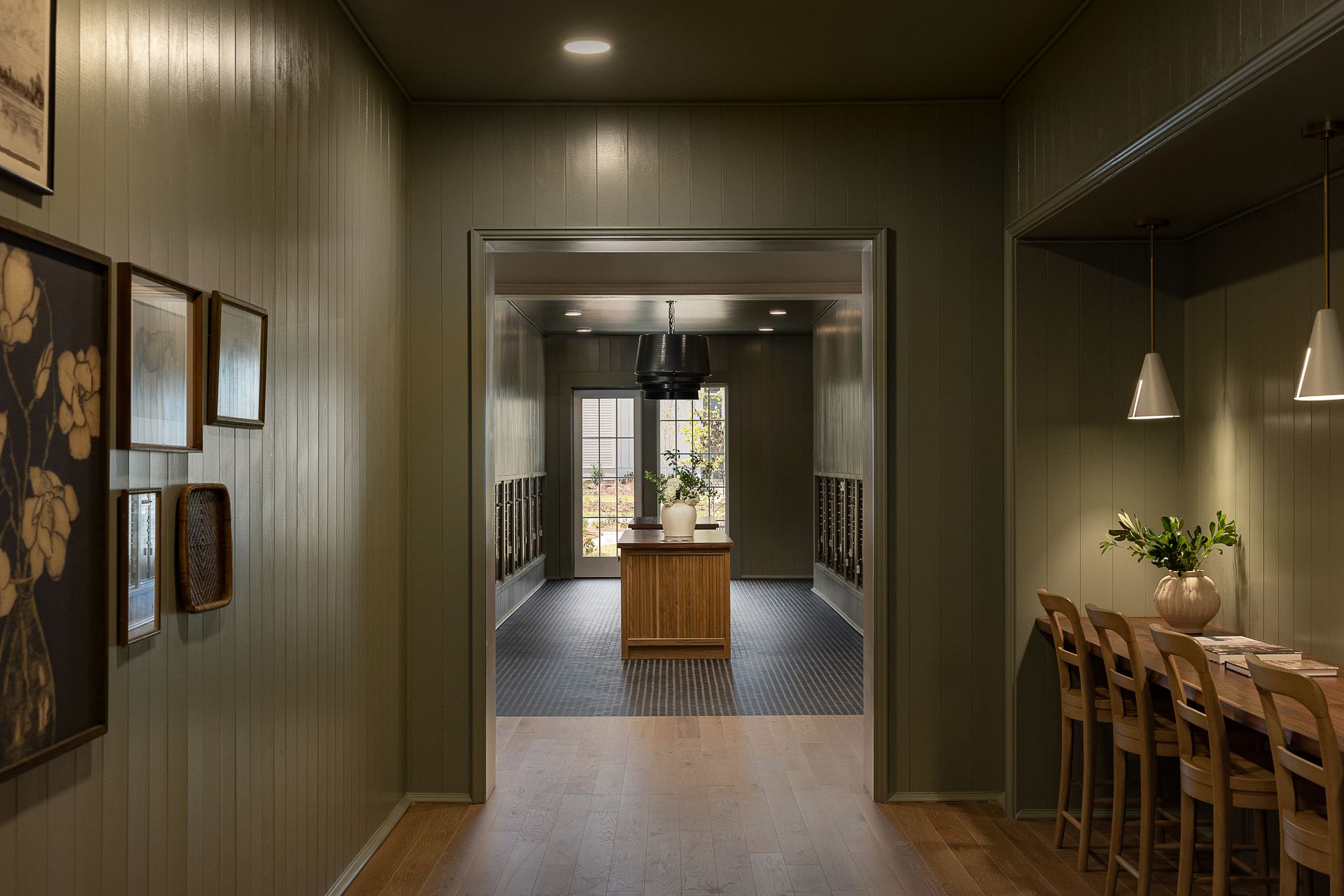Hallway with green walls, framed art, and doorway leading to a kitchen with an island and dining area with a table and chairs.