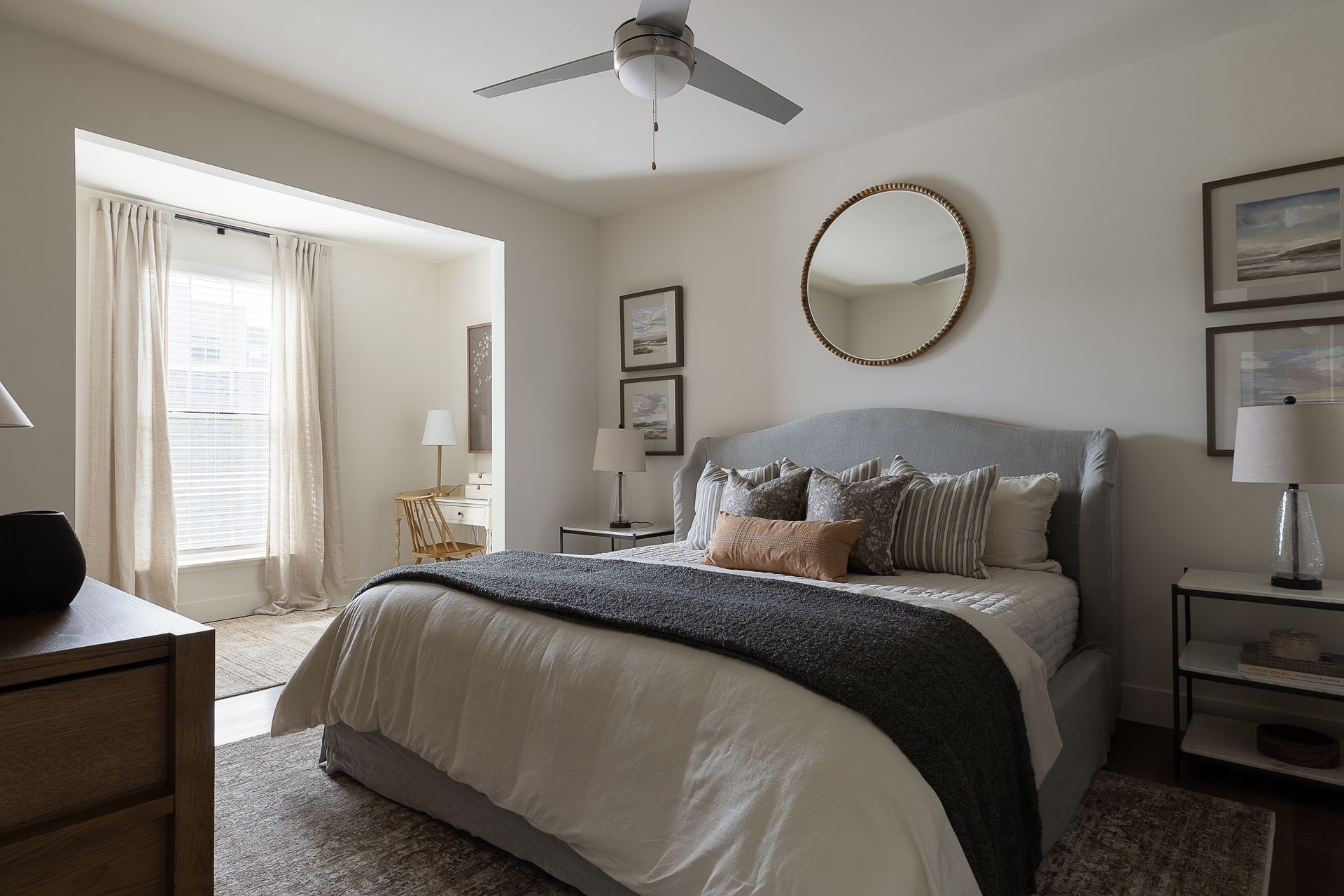Bedroom with a gray bed, round mirror, and neutral-toned decor.