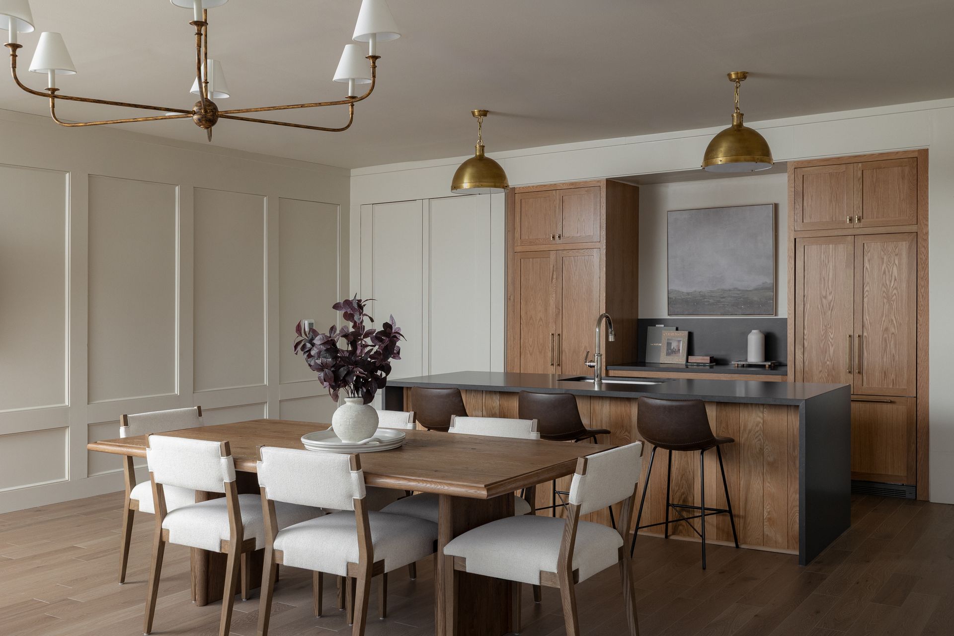 Dining area with light wood table, white chairs, and a kitchen with wooden cabinets and island.