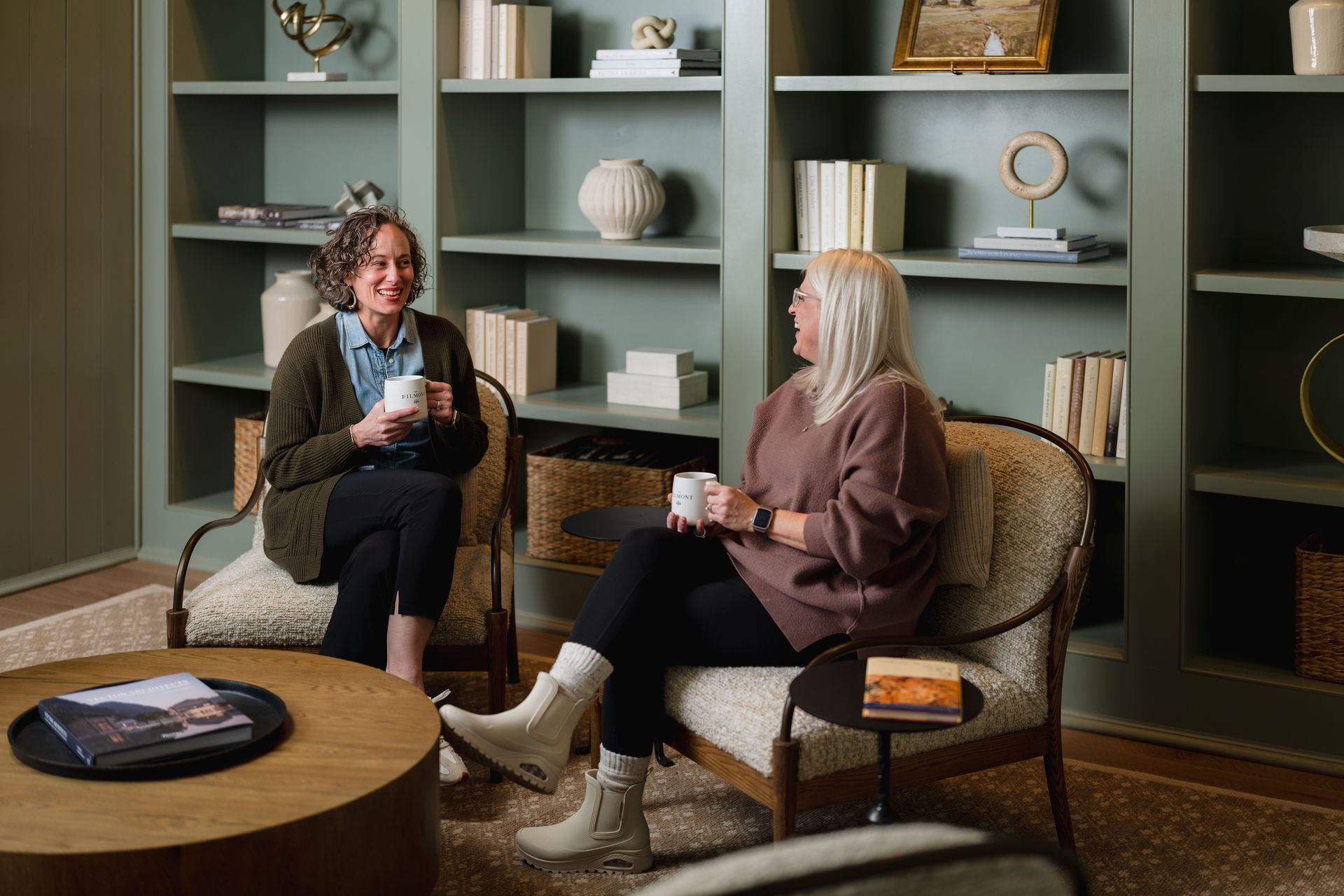 Couple seated on outdoor furniture, toasting with drinks. Gray wall with mural backdrop.