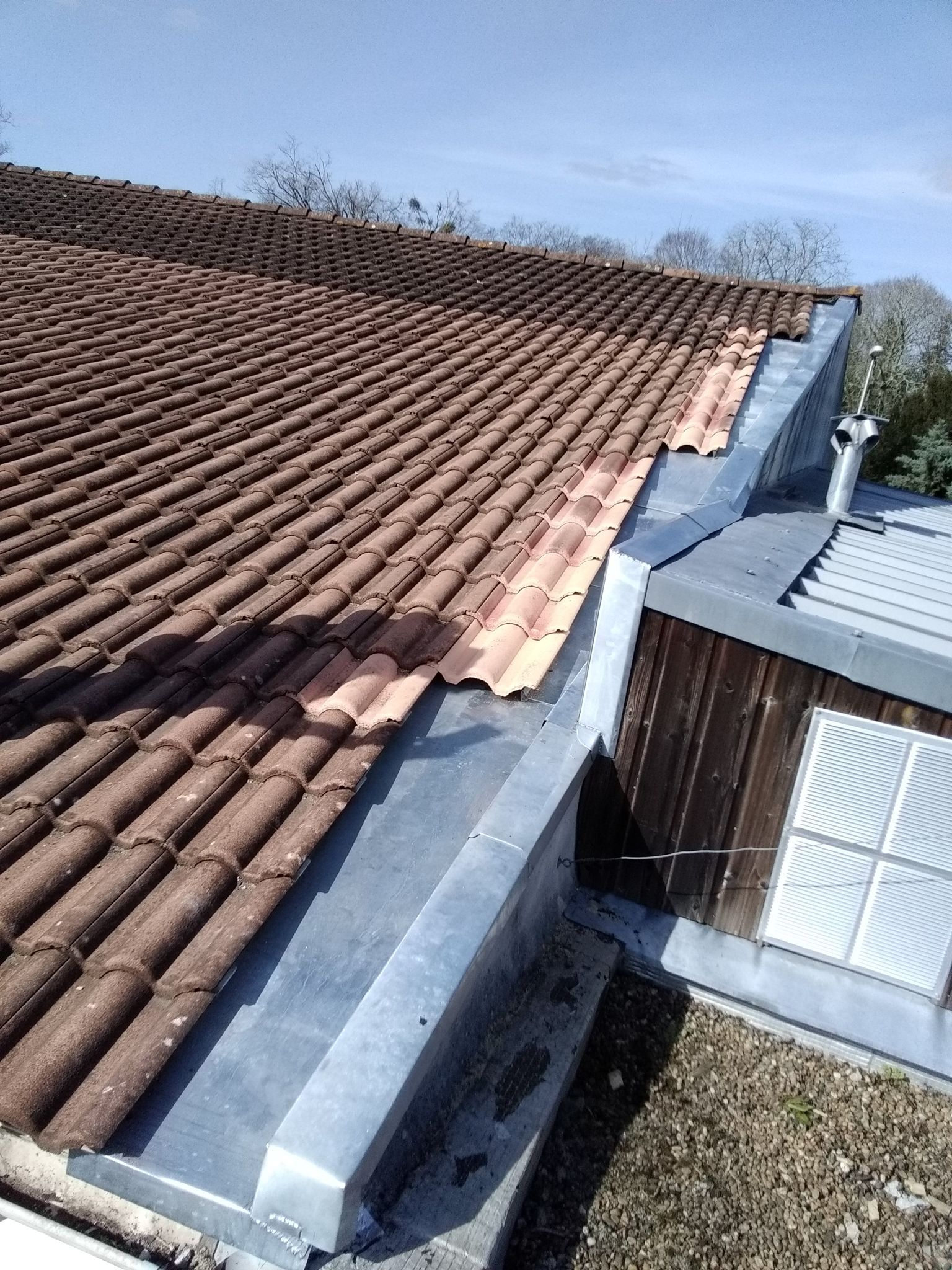 Un toit équipé d'une gouttière en métal, avec un bâtiment en bois en arrière-plan.