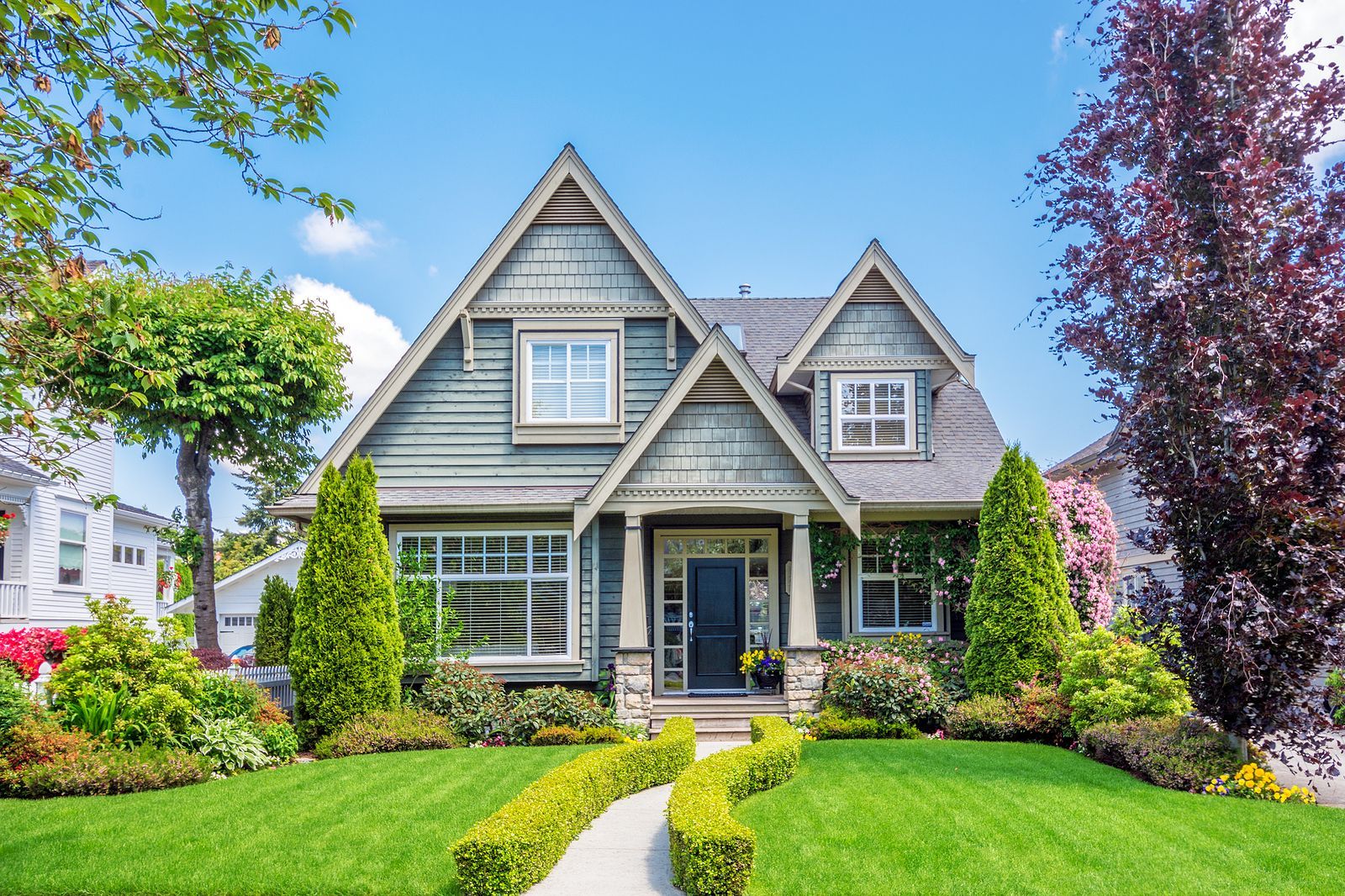 A teal-colored house with a manicured front lawn, a walkway, and lush landscaping under a sunny sky.