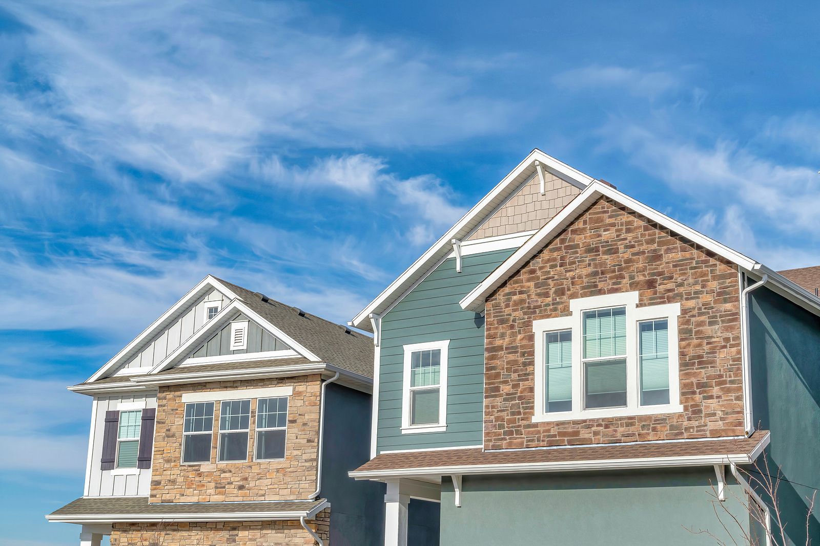 Two-story houses with blue and stone siding under a bright blue sky with wispy clouds.