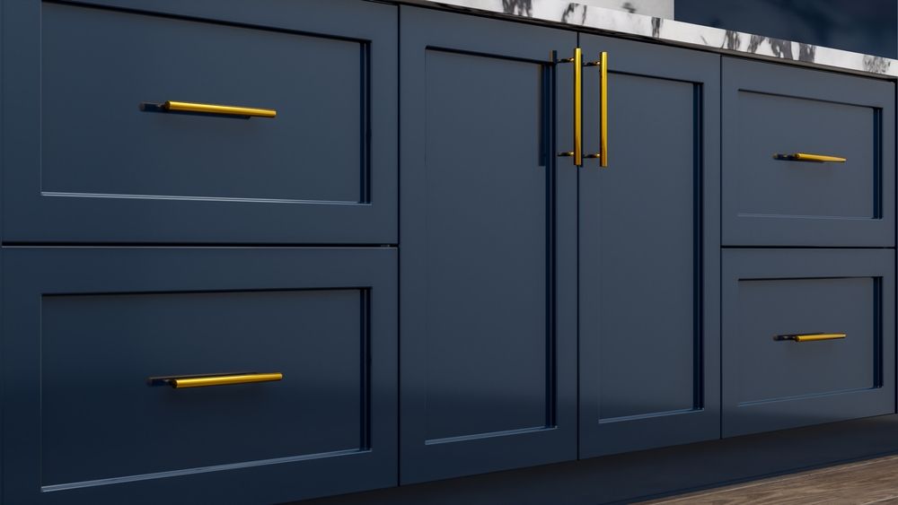 Close-up of dark blue kitchen cabinets with gold hardware. Drawers and doors are visible, with a white countertop above.