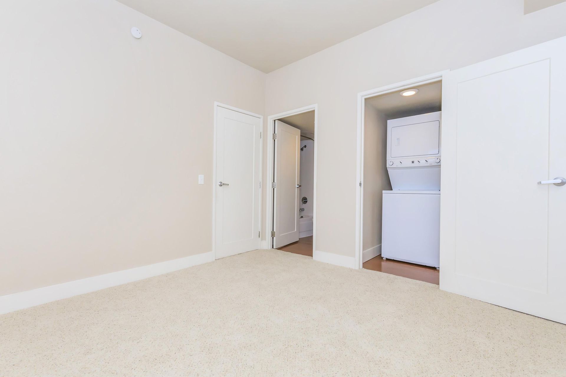 Empty bedroom with carpet, doors to bathroom and laundry closet, and neutral walls.