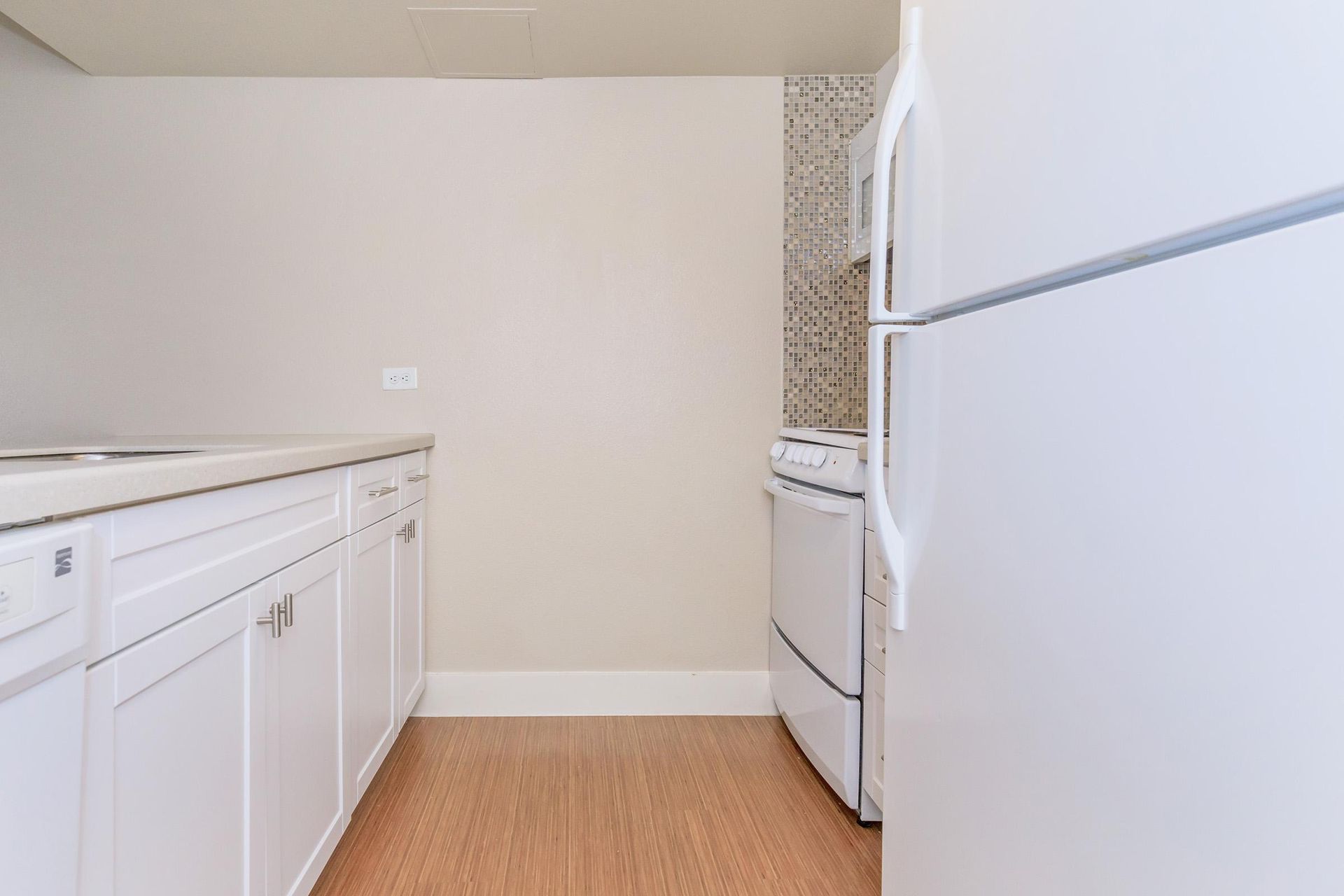White kitchen cabinets, refrigerator, and stove against a neutral wall; wood floor.