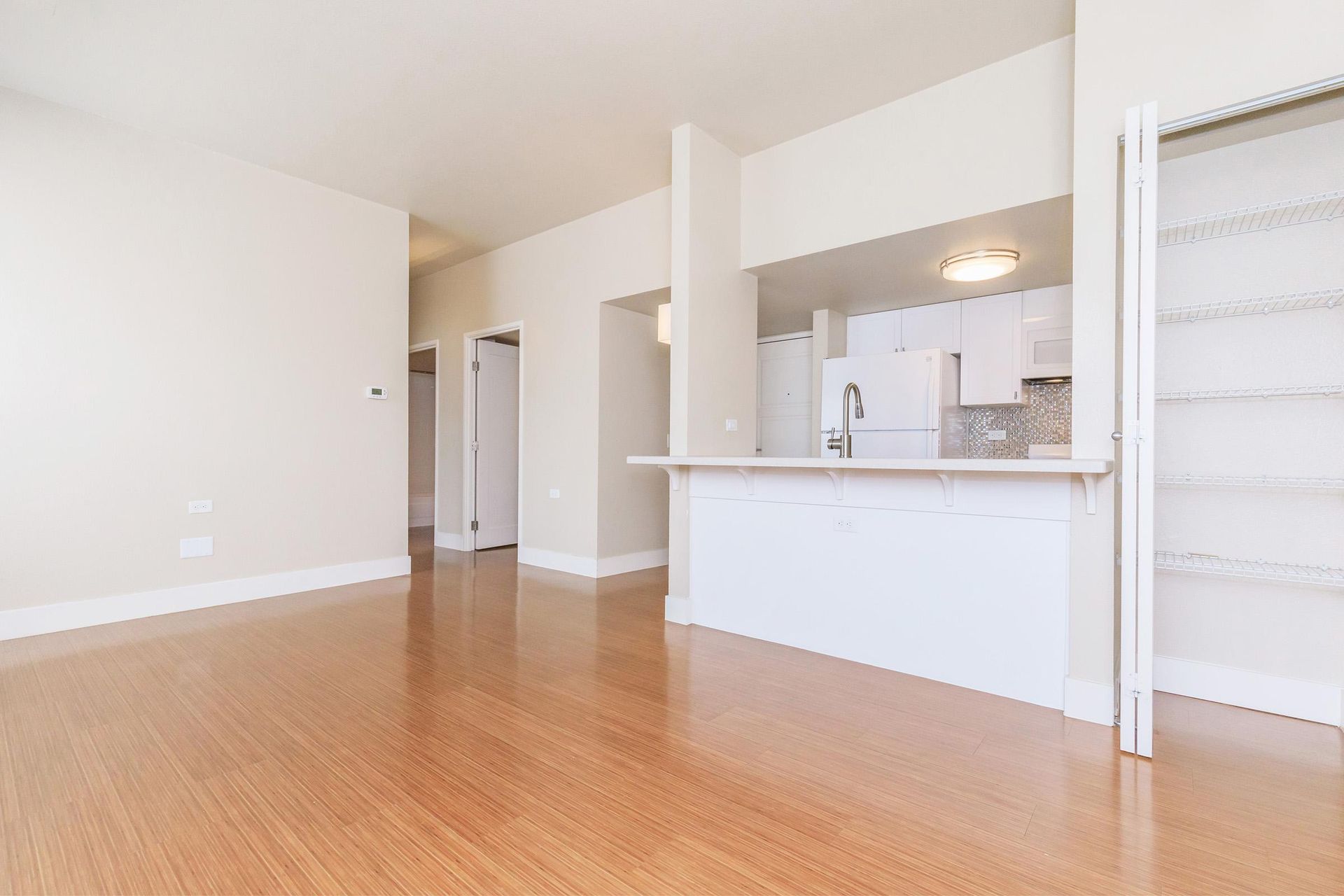 Empty apartment interior, featuring wood floors, white walls, and a kitchen with a breakfast bar.