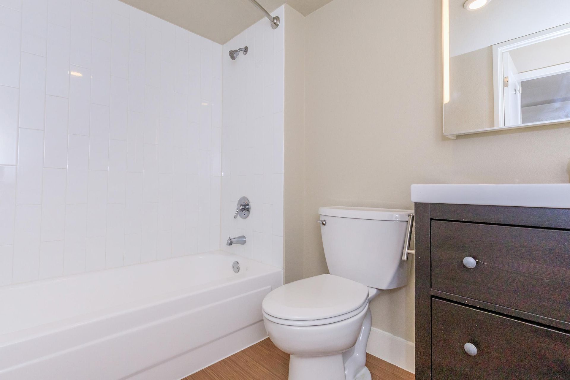 Bathroom with white bathtub/shower, toilet, and dark brown vanity; light beige walls.