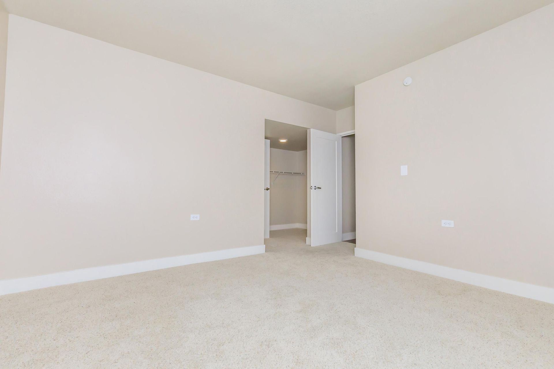 Empty bedroom with beige walls, carpet, and an open closet.