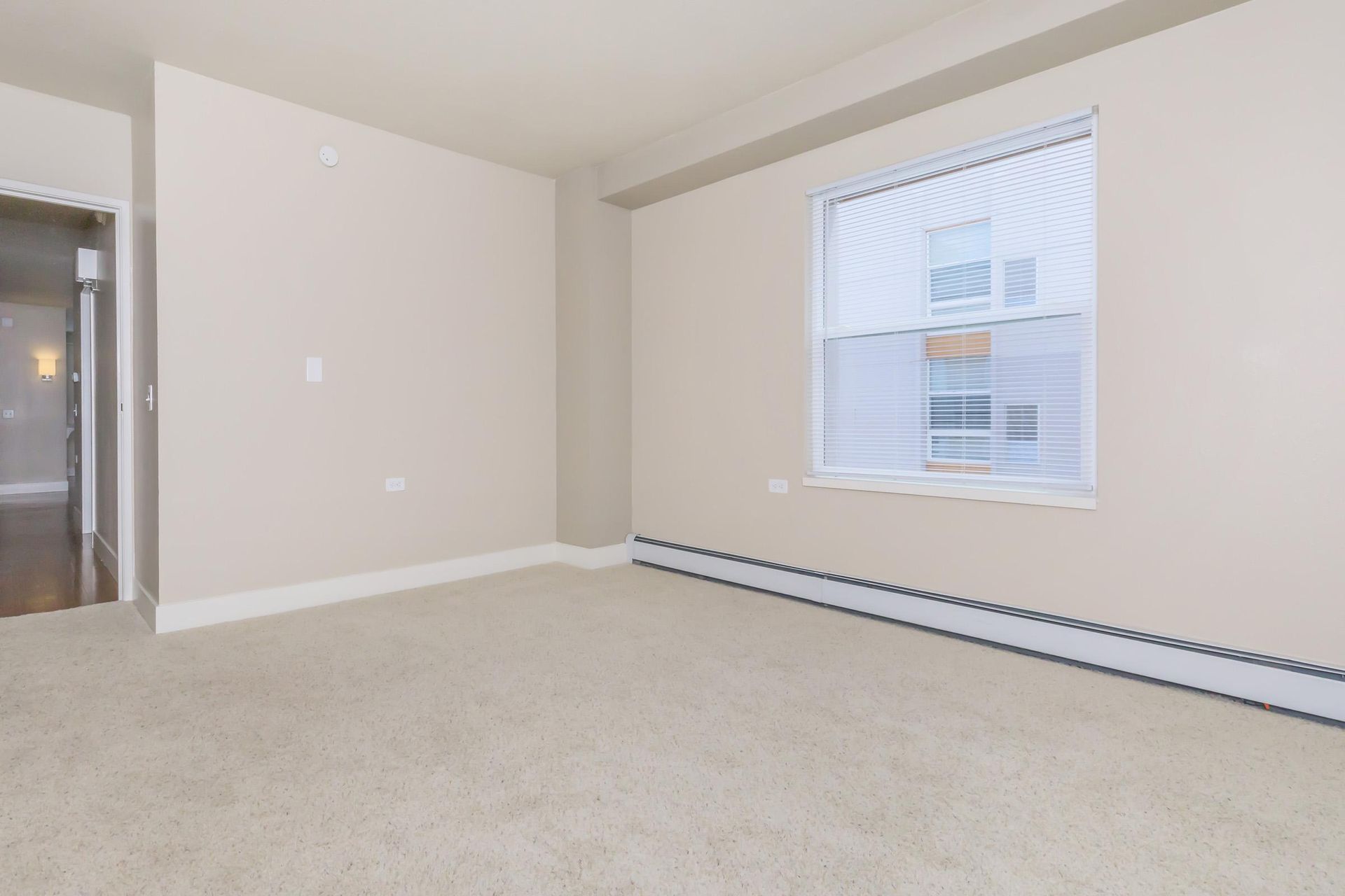 Empty beige carpeted room with a window and a doorway.