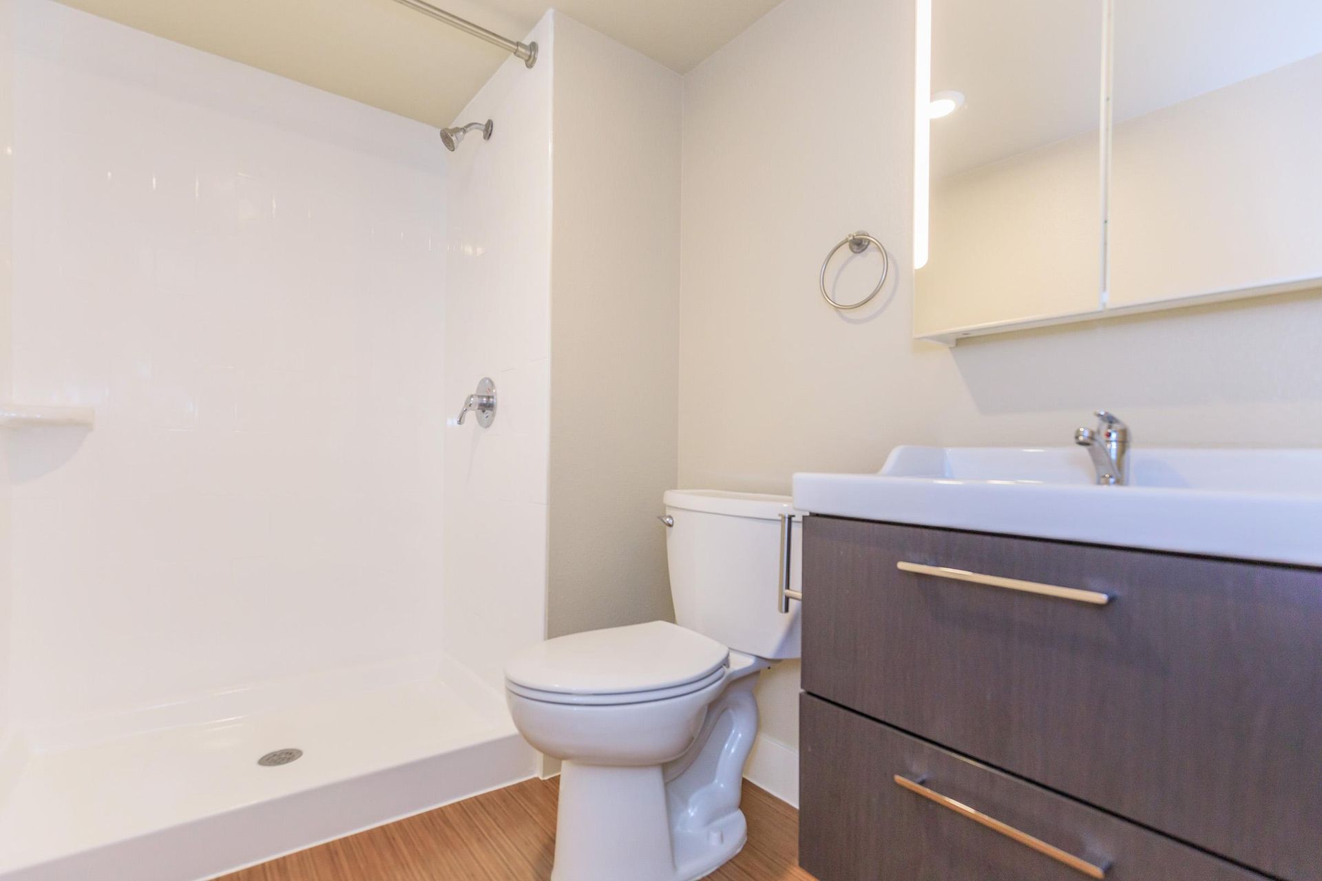 Bathroom with white shower stall, toilet, dark vanity, and wood-look floor.