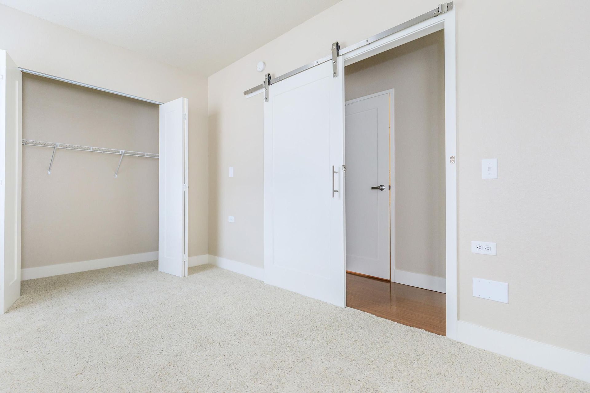 Empty bedroom with beige carpet, a closet, and a white sliding door.