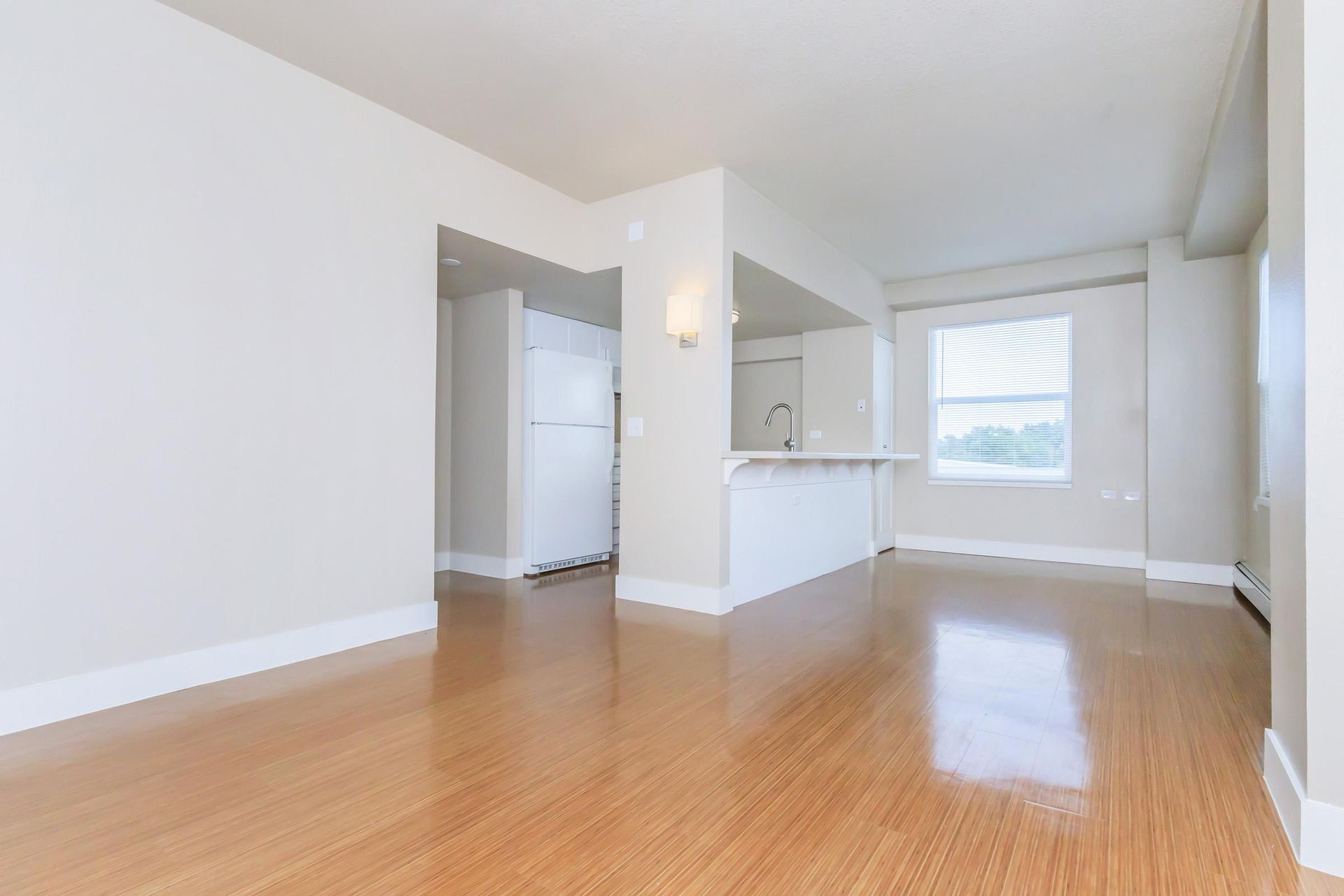 Empty bright apartment interior with hardwood floors, white walls, and a small kitchen.