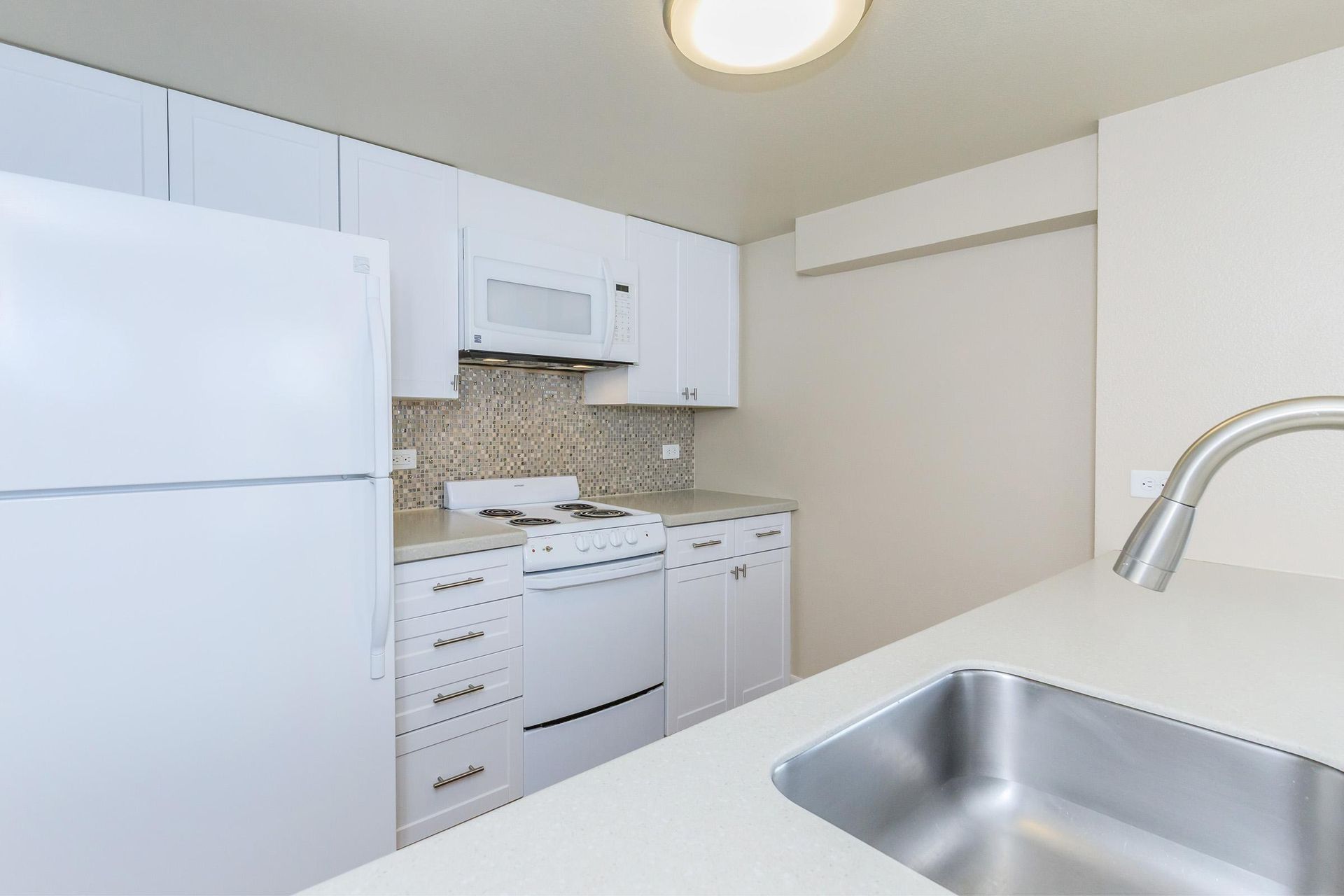 White kitchen with appliances including refrigerator, stove, dishwasher, and microwave. Sink in foreground.