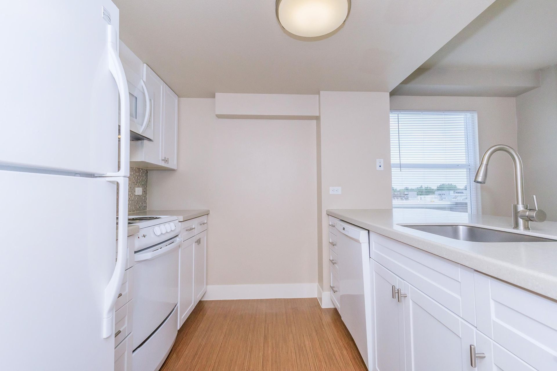 White kitchen with appliances, cabinets, and a sink by a window.
