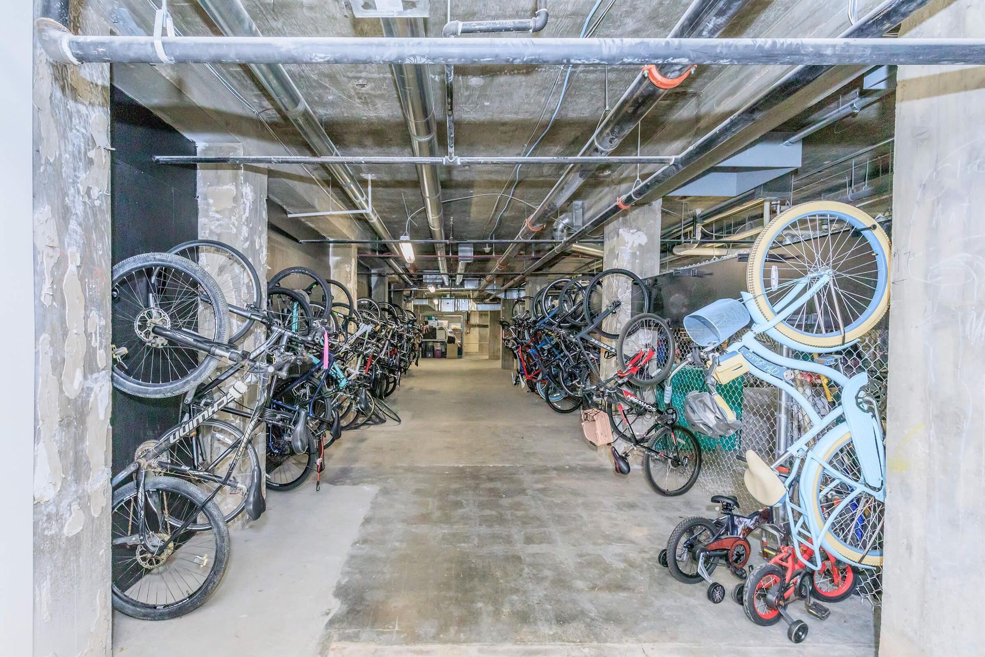 Bicycle parking area in a building, with multiple bikes hanging from racks on the wall.