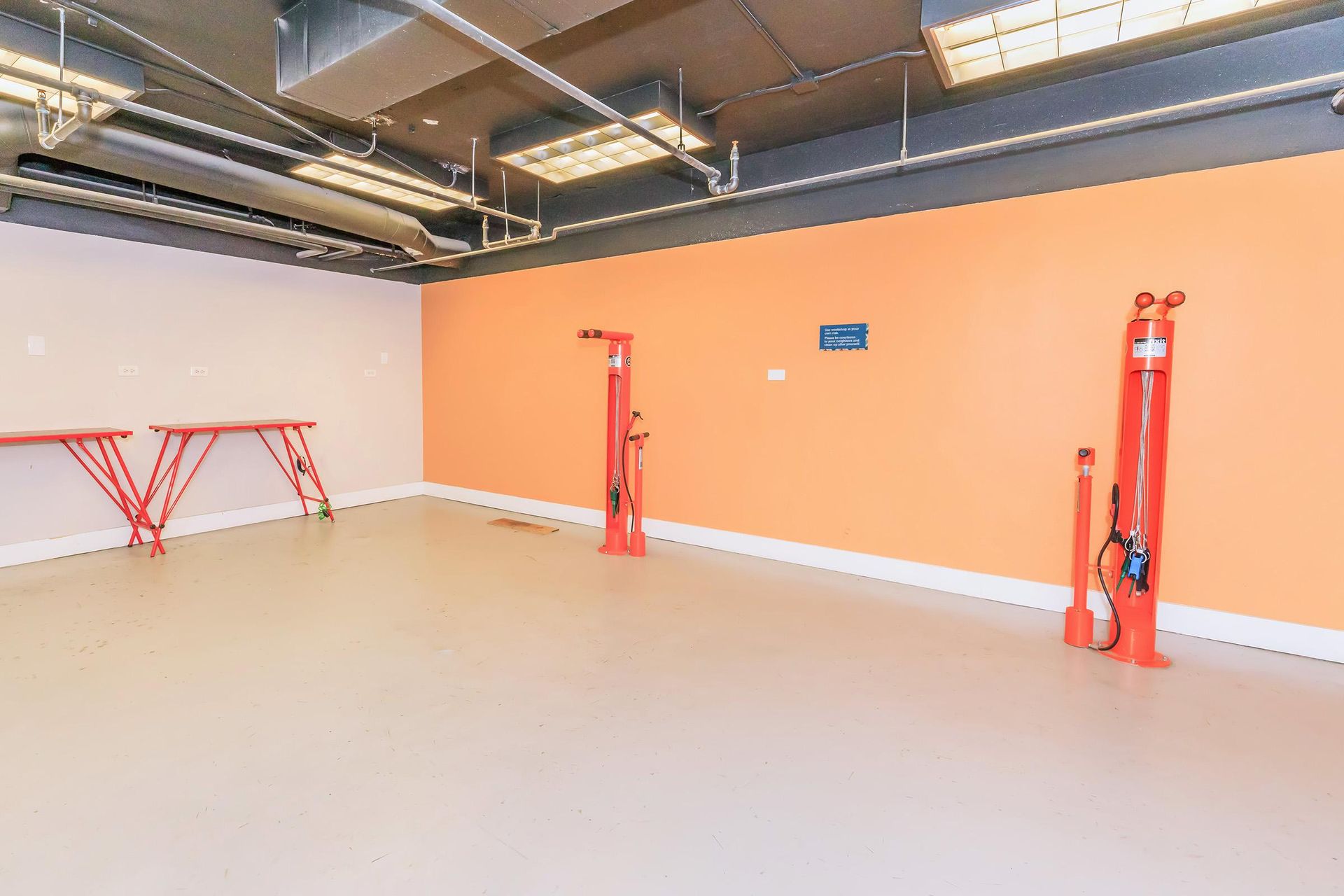 An empty, modern bike repair station with orange walls, red tools, and a beige floor.