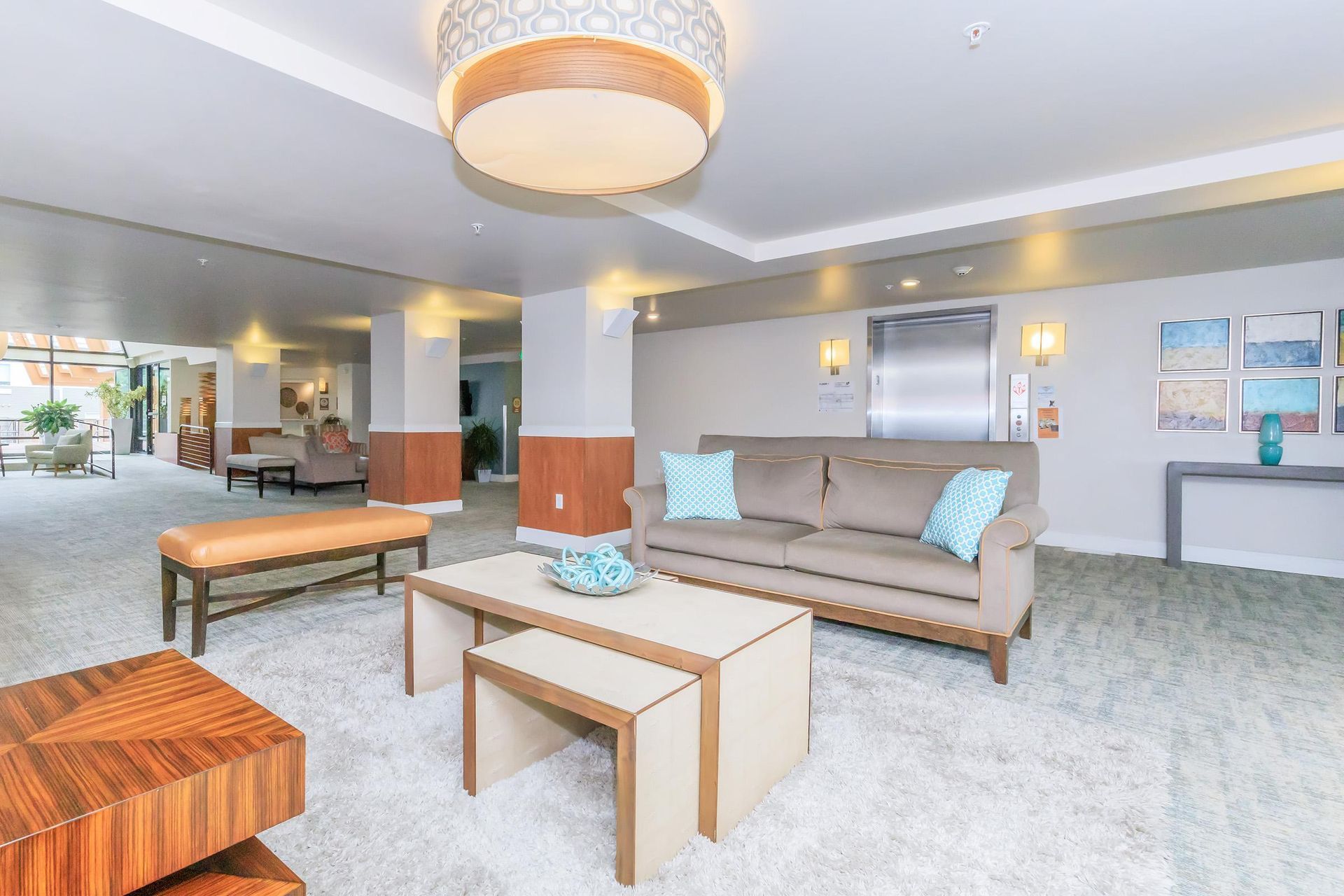 Lobby with a couch, coffee tables, and a bench; beige and blue color scheme, elevator in the background.