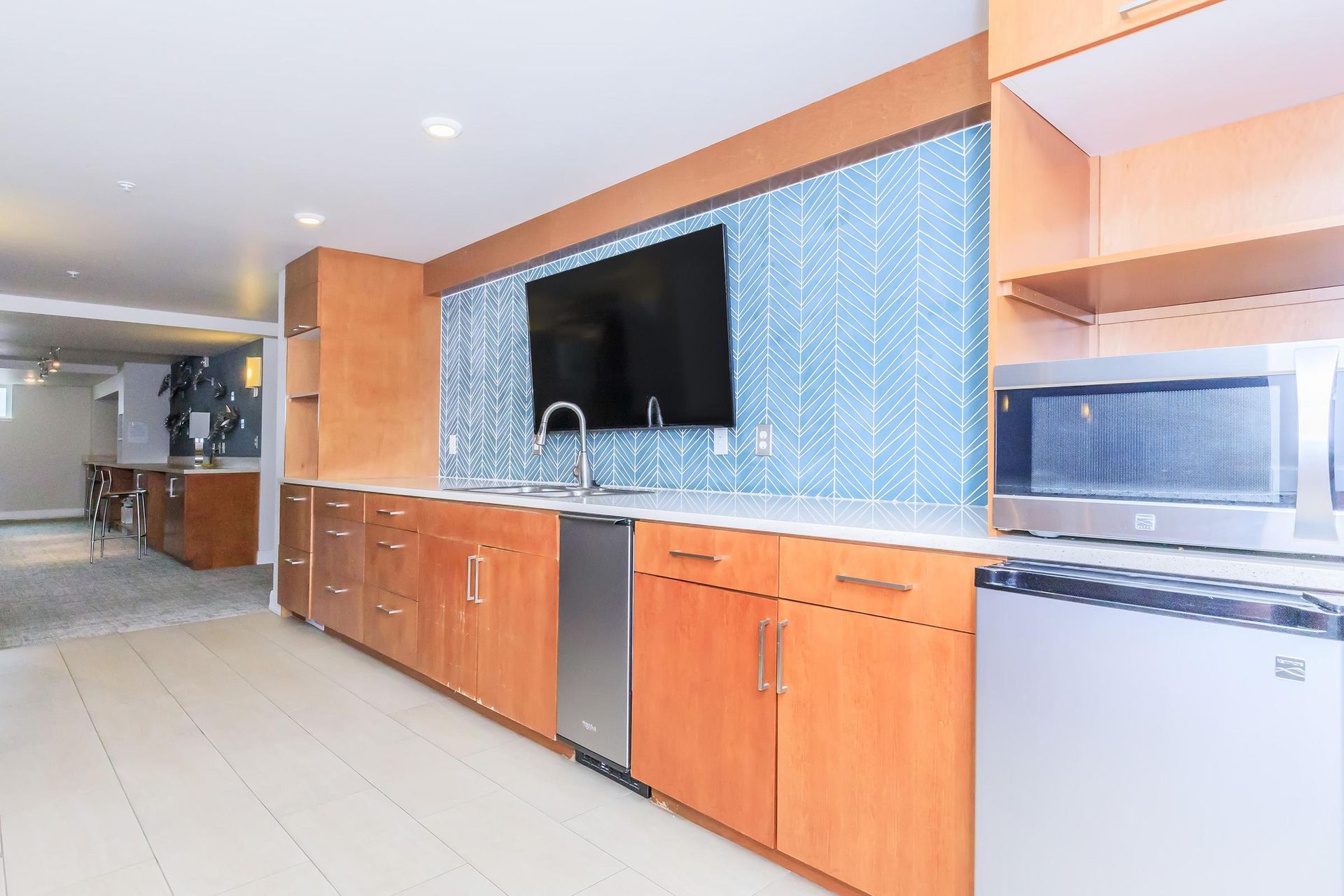 Modern kitchen with wooden cabinets, blue tile backsplash, TV, microwave, and sink.