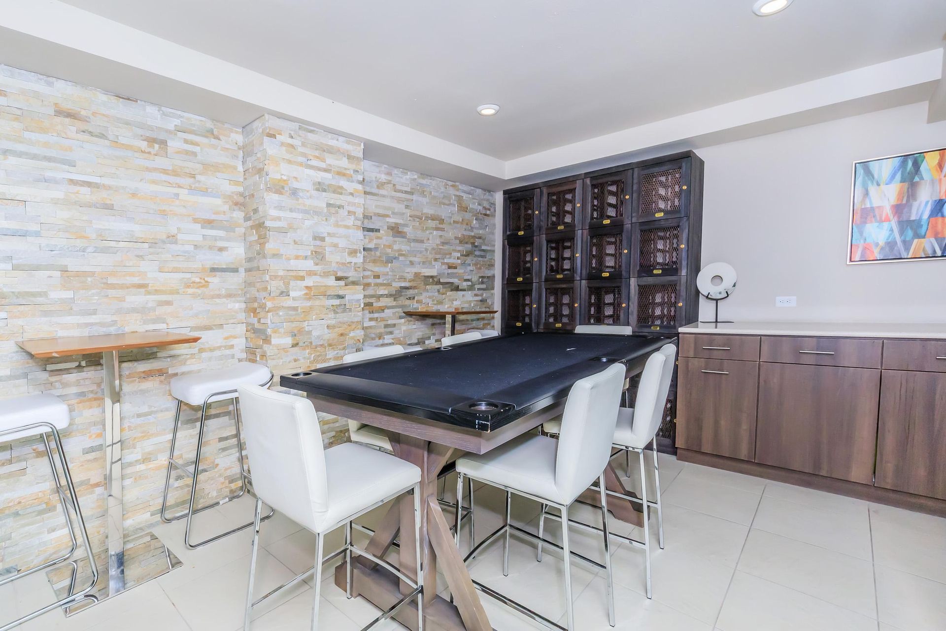 Game room with a pool table, bar stools, and cabinetry against a textured stone wall.