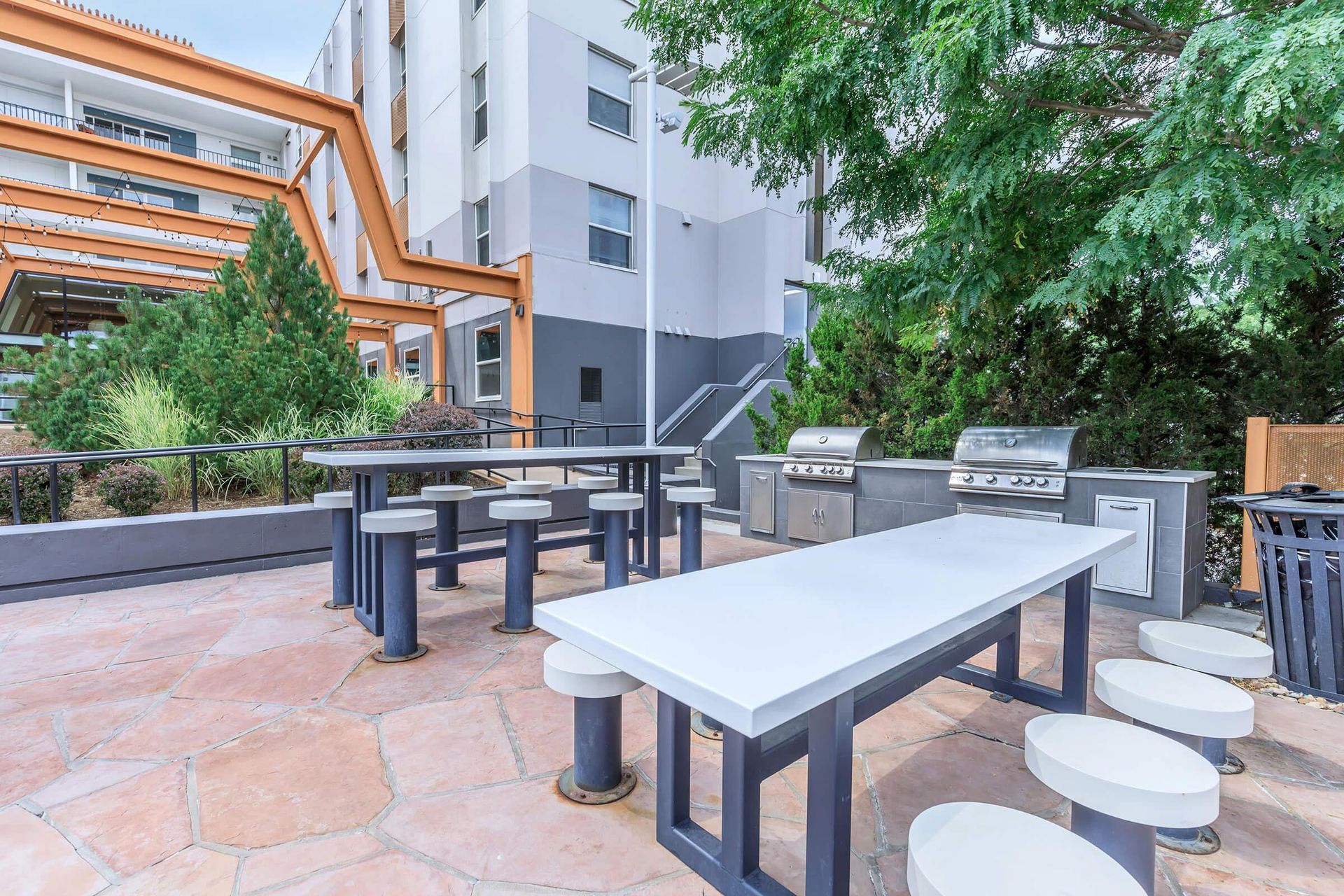 Outdoor grilling area with tables, stools, grills, and a modern building.