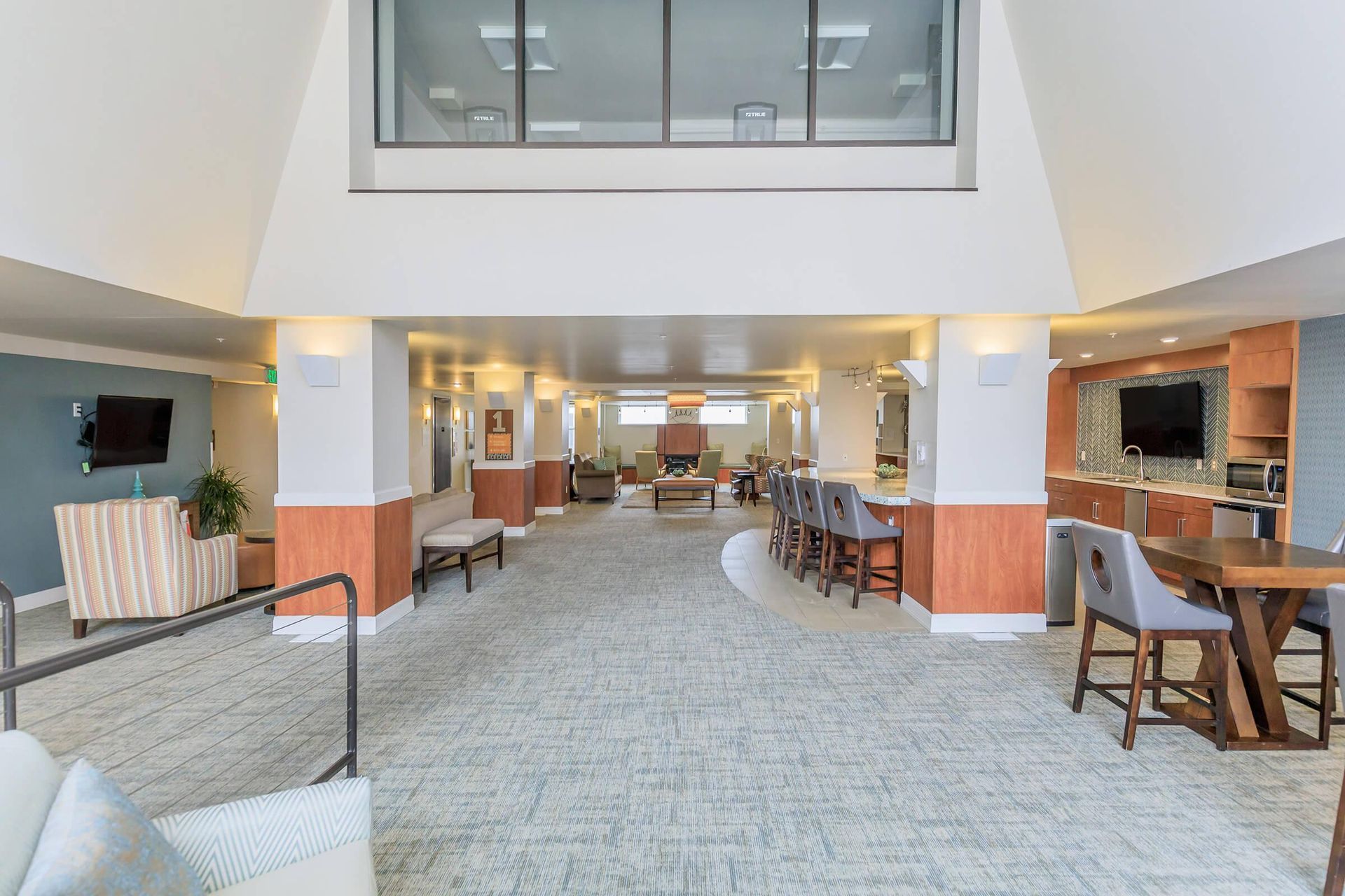 Spacious interior lobby with neutral colors, seating areas, a bar, and a television.